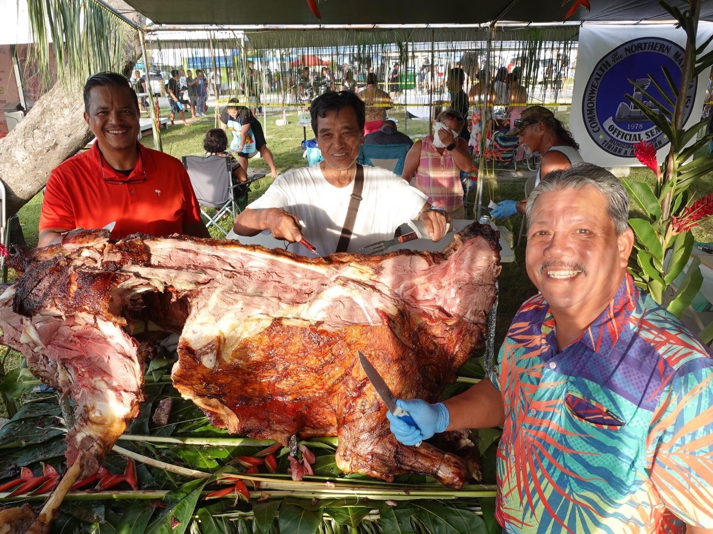 Tinian Mayor Edwin Aldan, right, and Sen. Jude U. Hofschneider are joined by a visitor in serving up a whole, barbequed cow at the 24th Annual Taste of the Marianas International Food Festival & Beer Garden on June 3, 2023, in Saipan.  The festival, organized by the Marianas Visitors Authority, is held every Saturday evening through June at Garapan Fishing Base.