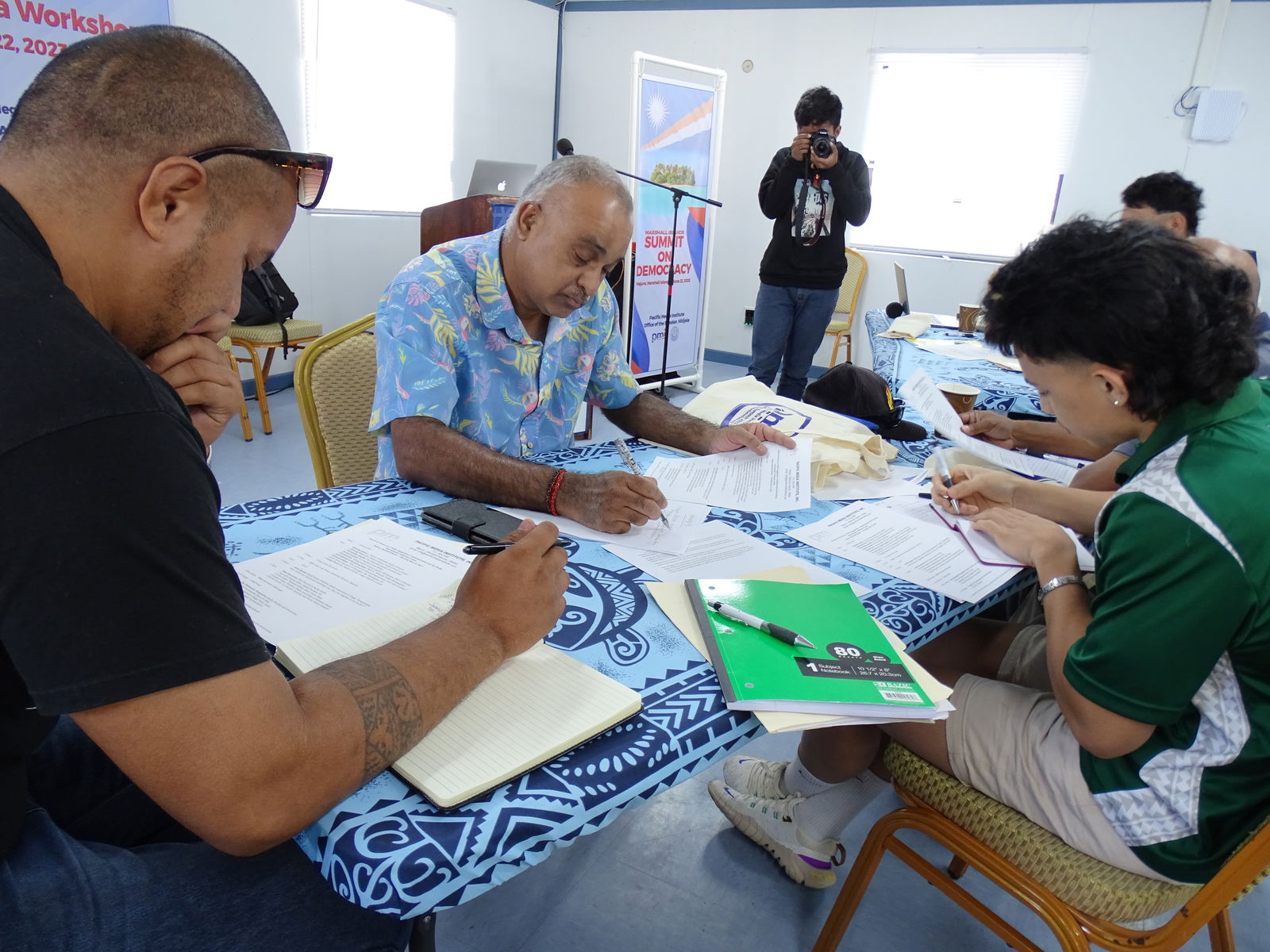 Majuro Media and Democracy Workshop participants Absolom Harris, left, and Yale Kramer, right, work on news assignments with veteran journalist Anish Chand, the west bureau chief for the Fiji Times.