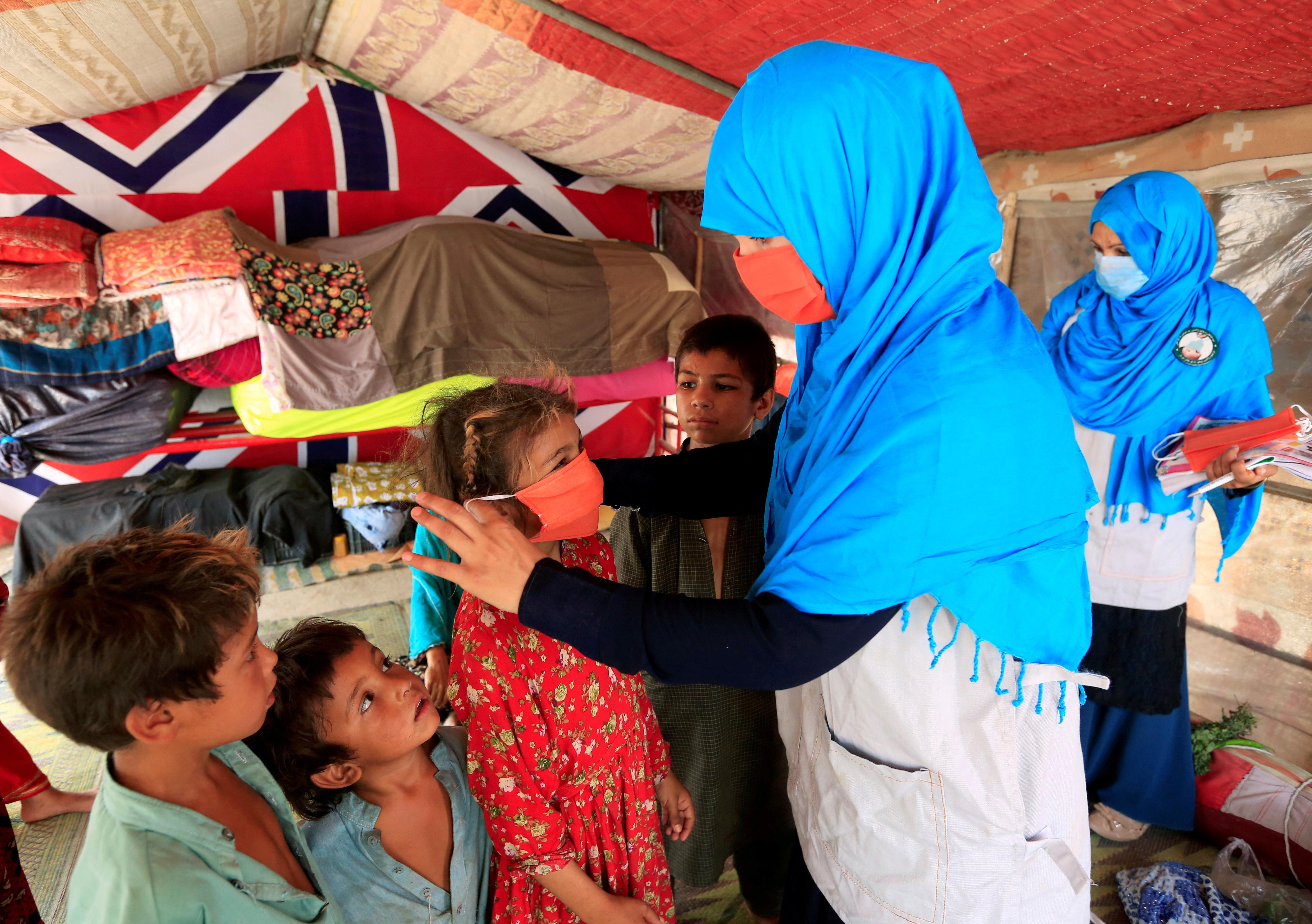 FILE PHOTO: A UNICEF worker helps an internally displaced girl put on a face mask at a makeshift camp, amid the pandemic, in Jalalabad, Afghanistan June 22, 2020. REUTERS/Parwiz/File Photo