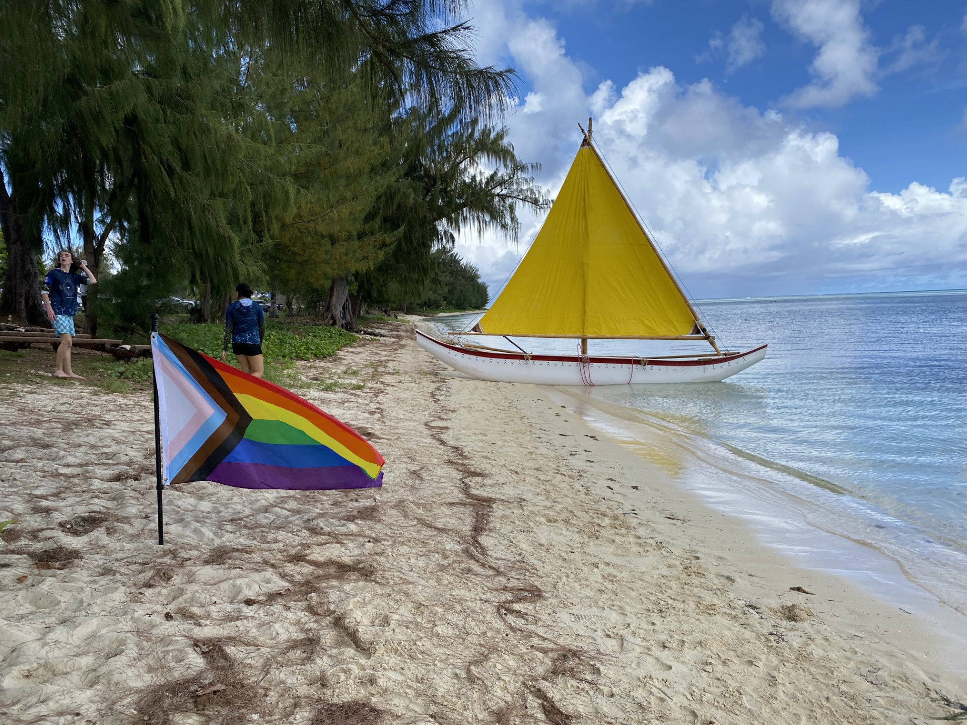 Aunty Oba rests in the background as a pride flag flies on the 500 Sails Guma Sakman beach.