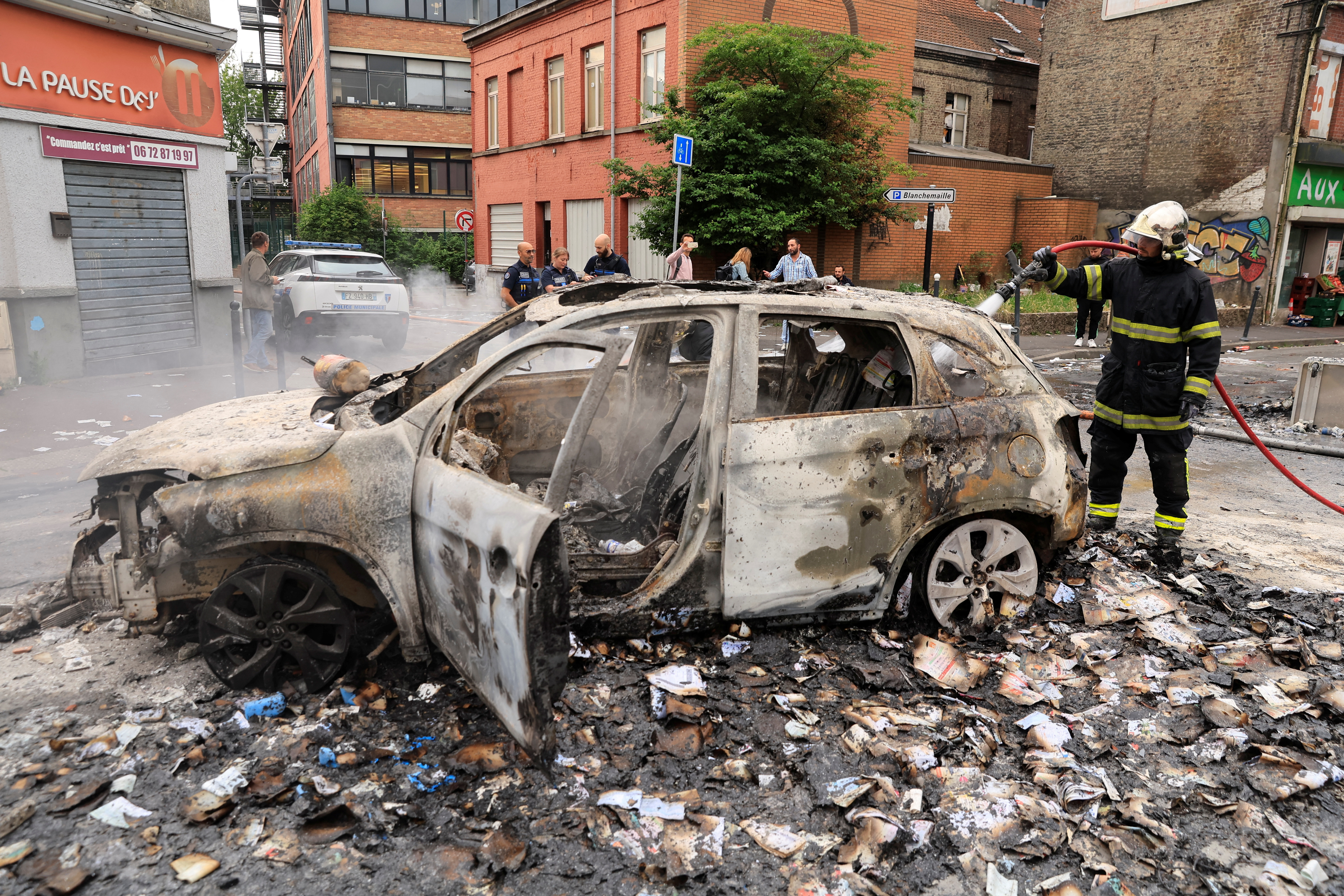 Firefighters extinguish fire from a car, burnt during night clashes between protesters and police, following the death of Nahel, a 17-year-old teenager killed by a French police officer in Nanterre during a traffic stop, at the Alma district in Roubaix, northern France, June 30, 2023. REUTERS/Pascal Rossignol