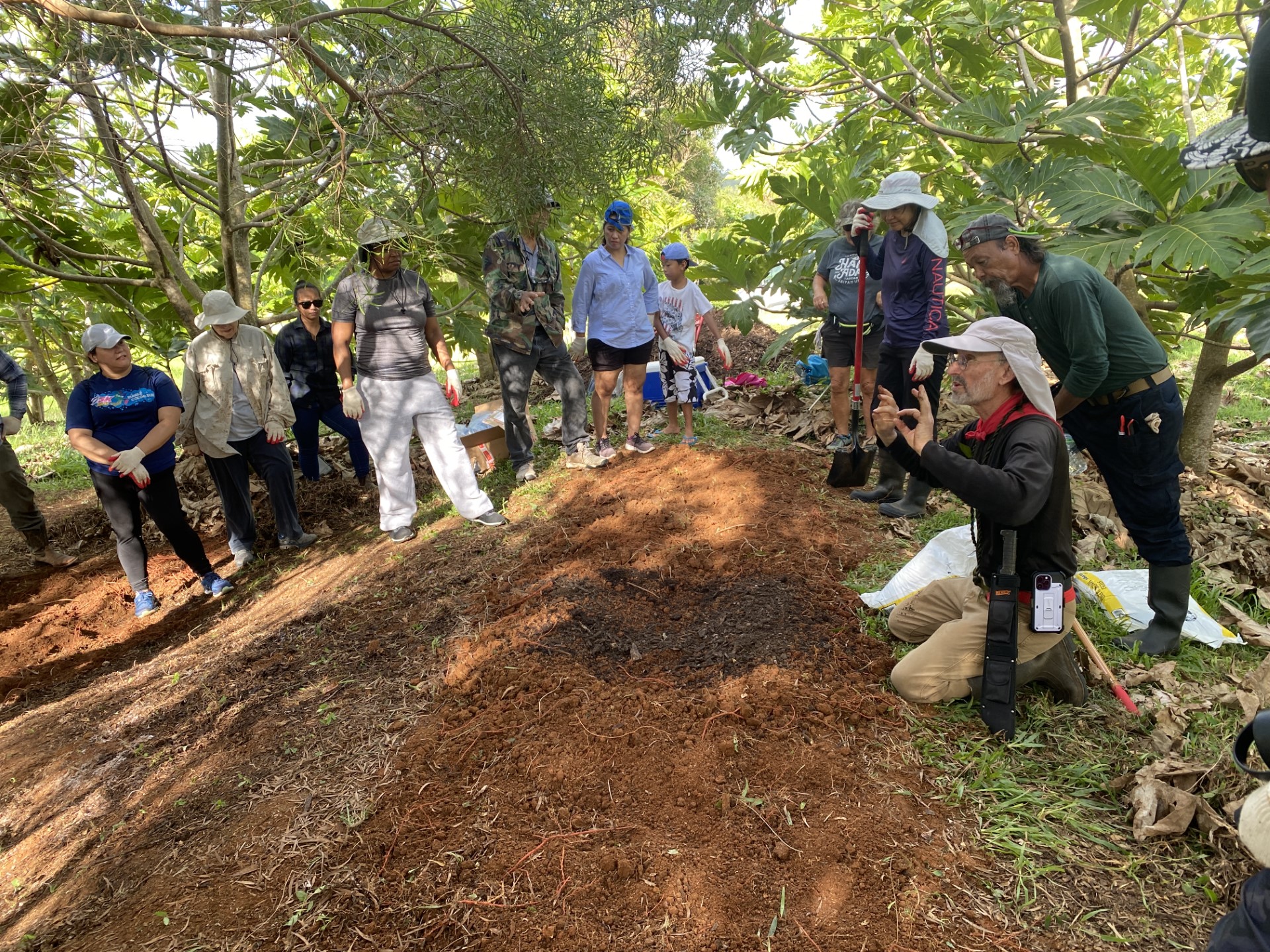 Dr. Craig Elevitch, kneeling, right, teaches participants about agroforestry at a recent workshop. Students pictured spent about 20 minutes preparing the garden bed in front of Elevitch. Out of the picture frame is another garden bed.