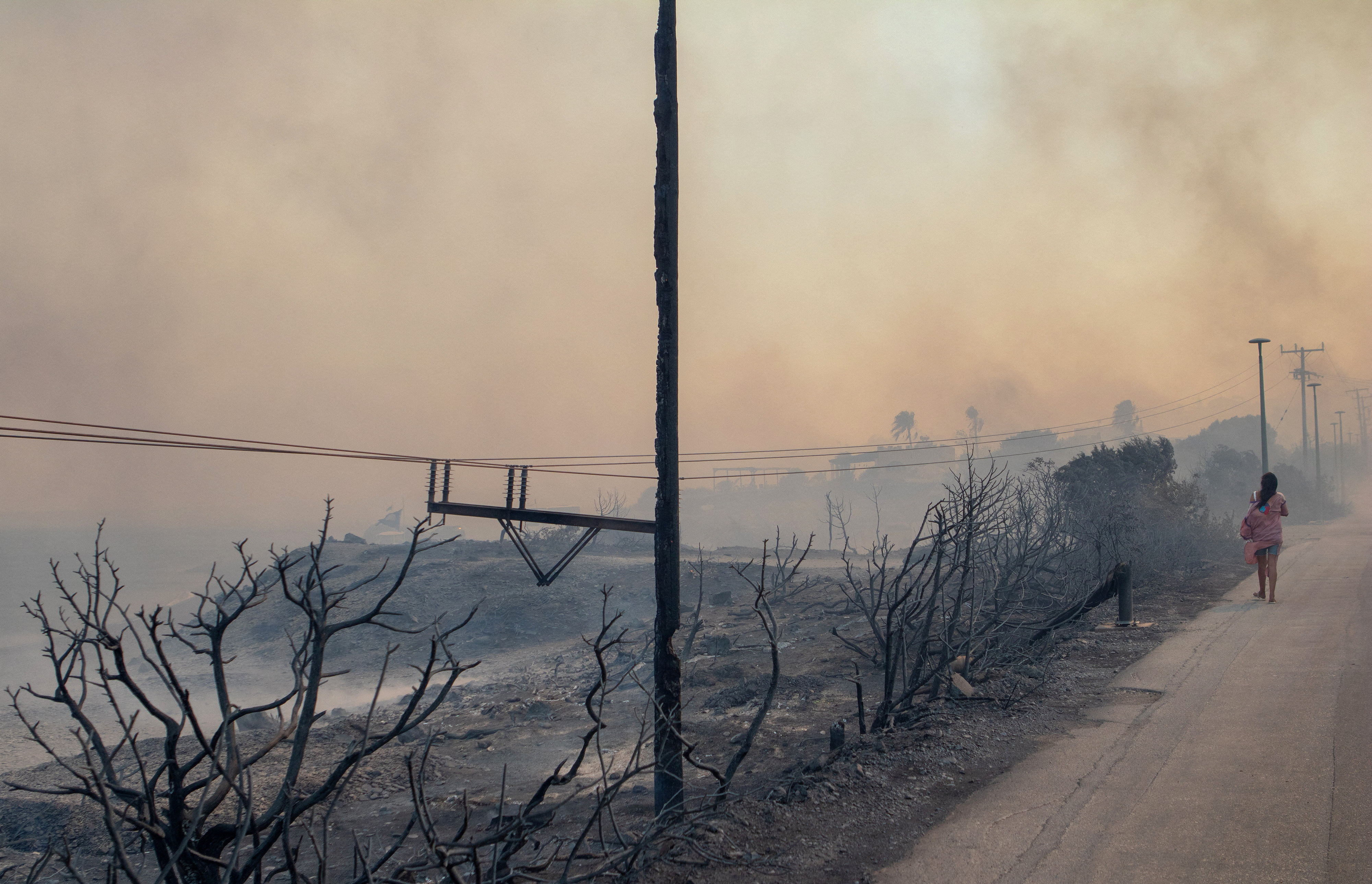 A person walks amidst smoke rising from wildfire burning near Lindos, on the island of Rhodes, Greece, July 22, 2023. REUTERS/Lefteris Damianidis