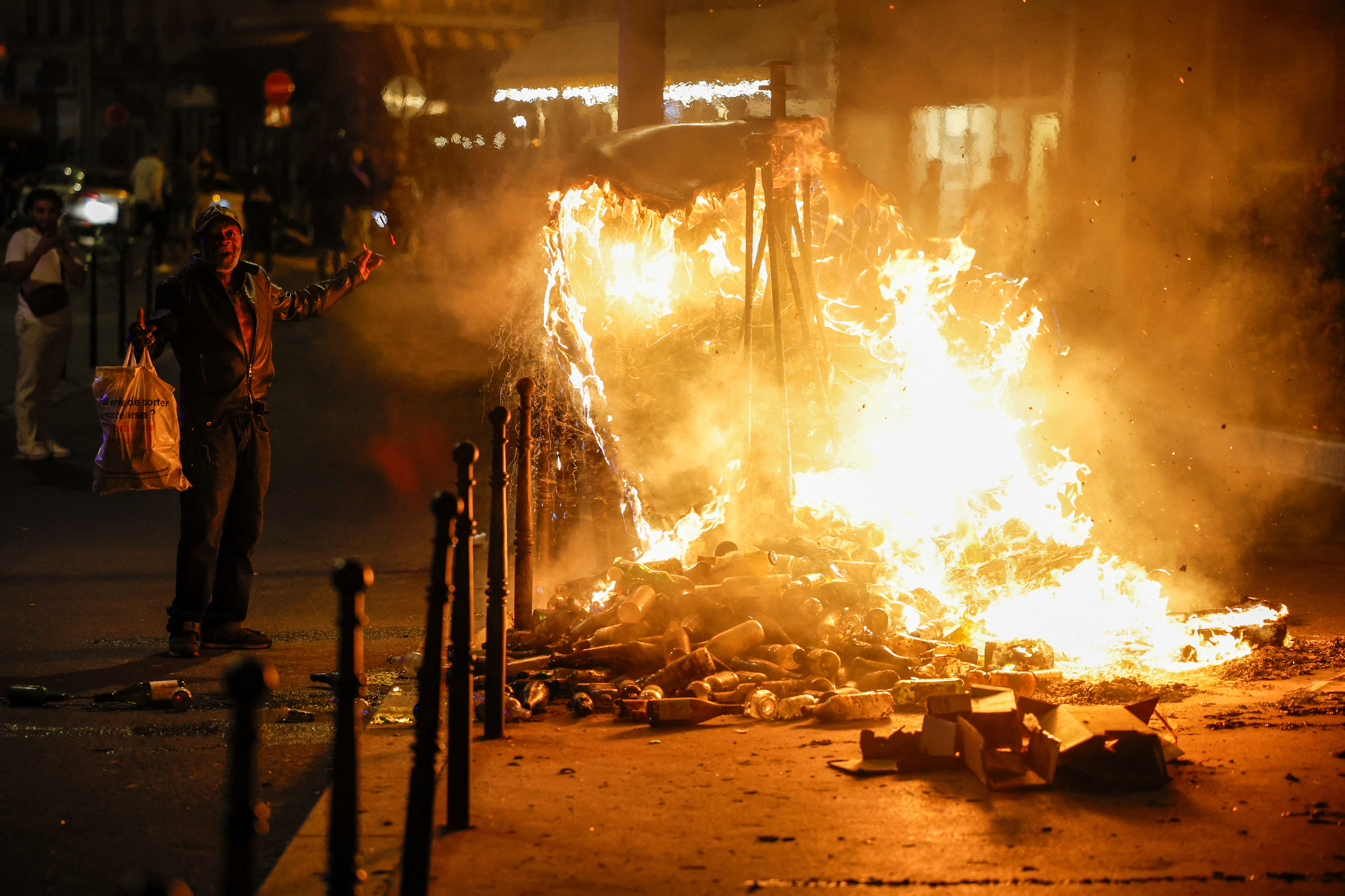 A man gestures next to a burning container as people protest following the death of Nahel, a 17-year-old teenager killed by a French police officer in Nanterre during a traffic stop, and against police violence, in Paris, France, June 30, 2023. REUTERS/Juan Medina