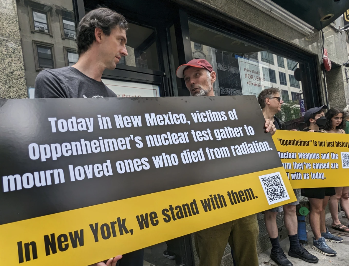 Matthew Bolton, left, and Jan-Christoph Zoels, center, hold a sign while rallying in New York City on July 15, 2023. The rally proceeded a screening and panel discussion on the new film, “Oppenheimer.”