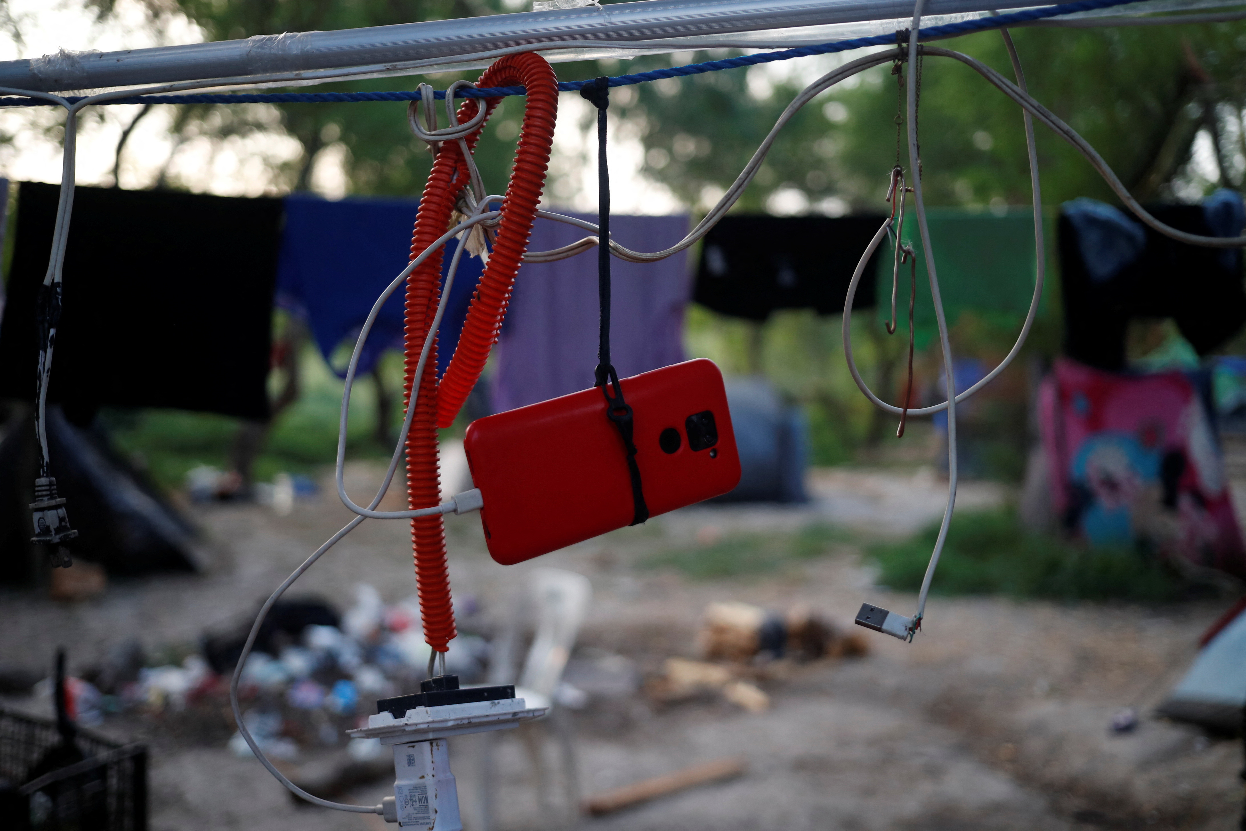 An asylum seeker hangs his cellphone on a rope while recharging the battery, while he waits to attempt to cross into the U.S. by an appointment through the Customs and Border Protection app, called CBP One, at a makeshift camp, in Matamoros, Mexico June 21, 2023. President Joe Biden promised to replace the hardline policies of former President Donald Trump, including the COVID-era public health order Title 42, with a more humane immigration system. The new Biden regulation allows migrants once again to ask for asylum at the border, but wait in Mexico for a slot on the app or risk a sped-up deportation process that could be conducted while they are held in detention. But in the first month of the new policy, Reuters found tens of thousands of people are waiting in dangerous Mexican border towns to snag a spot on the app, according to U.S. and Mexican officials, amid warnings from humanitarian groups of deteriorating sanitary conditions at migrant camps. REUTERS/Daniel Becerril