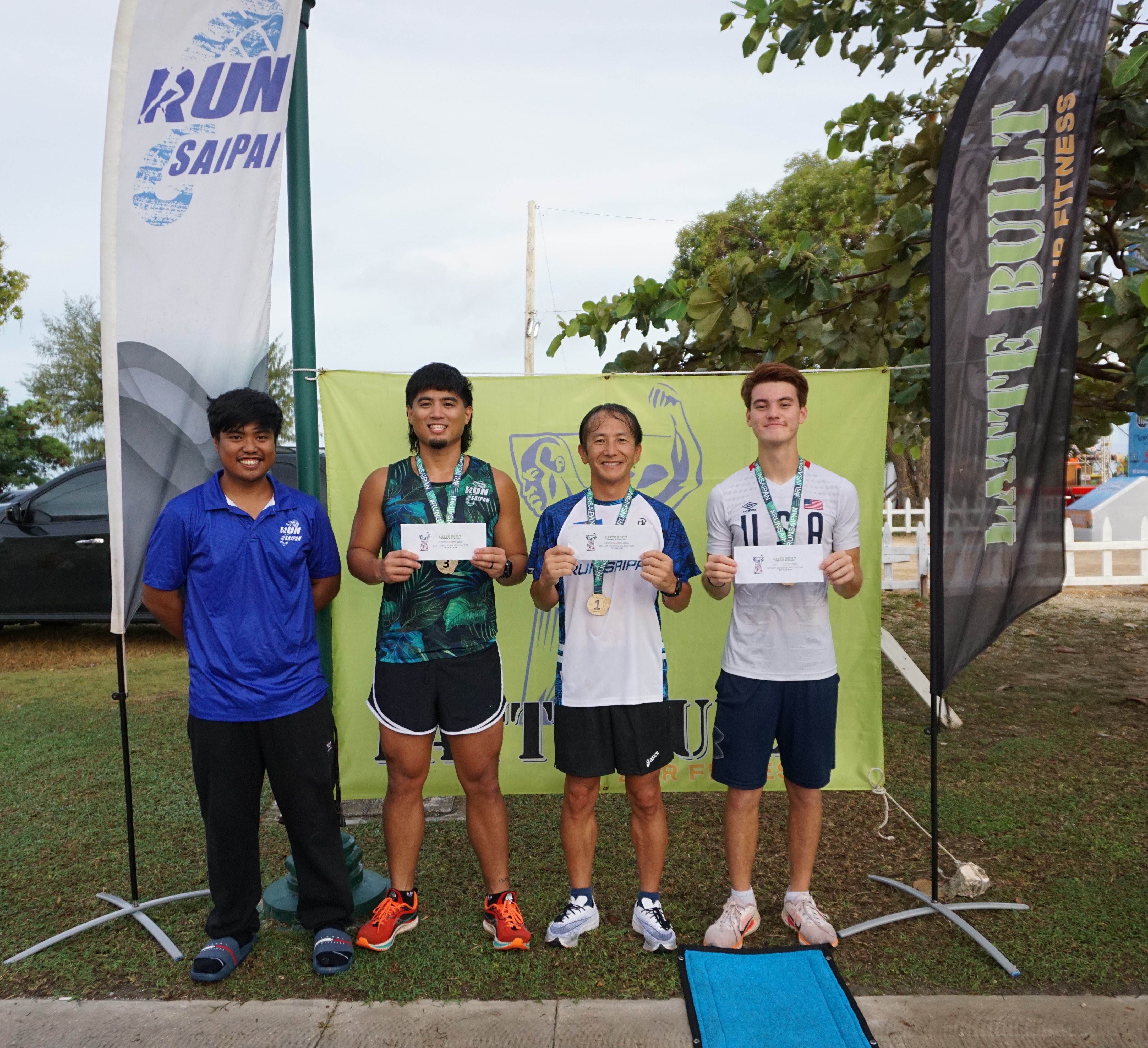 The top three men's division winners pose for a photo with Run Saipan tournament coordinator Simon Necesito during the awards ceremony for the 3rd Annual 4th of July Independence Day 2-Mile Run on Tuesday morning at the Garapan Fishing Base.
