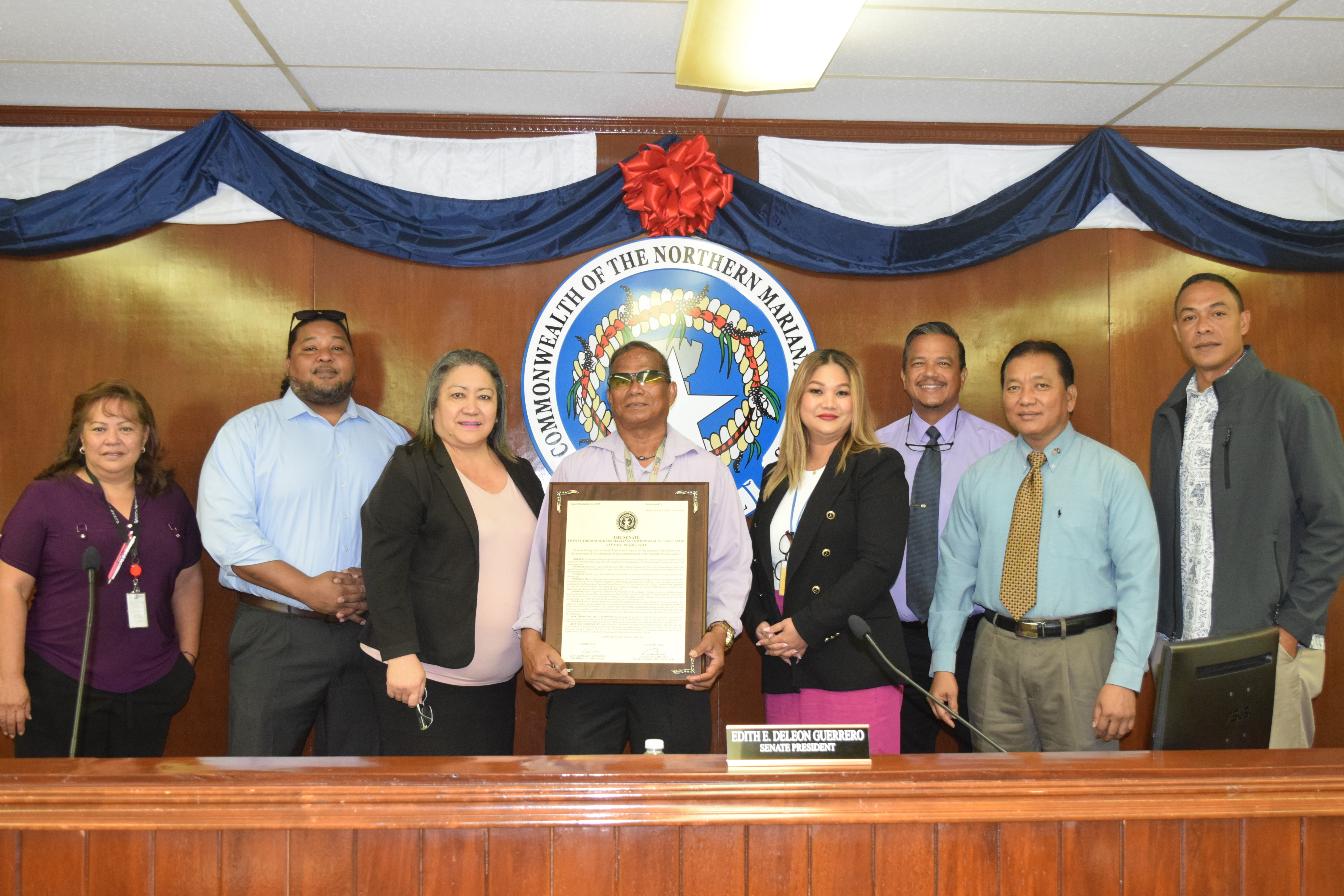 Marcelino “Max” Aguon, center, poses for a photo with senators on Friday as he holds a framed copy of a Senate resolution commending and recognizing his voluntary work in beautifying the environment.