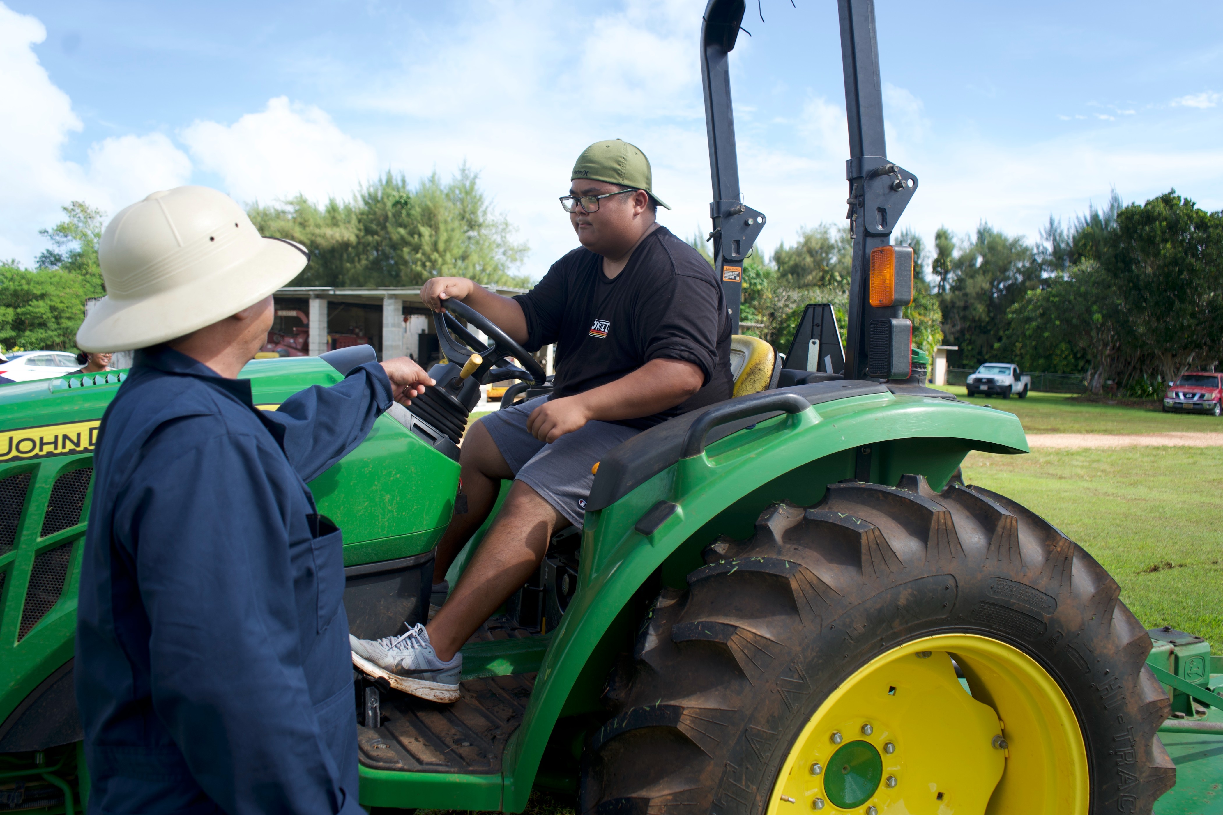 UOG student Ethan Umagat gets direction from agricultural research technician Frankie Matanane while learning to drive a tractor on Nov. 30, 2022, on Triton Farm in Yigo.