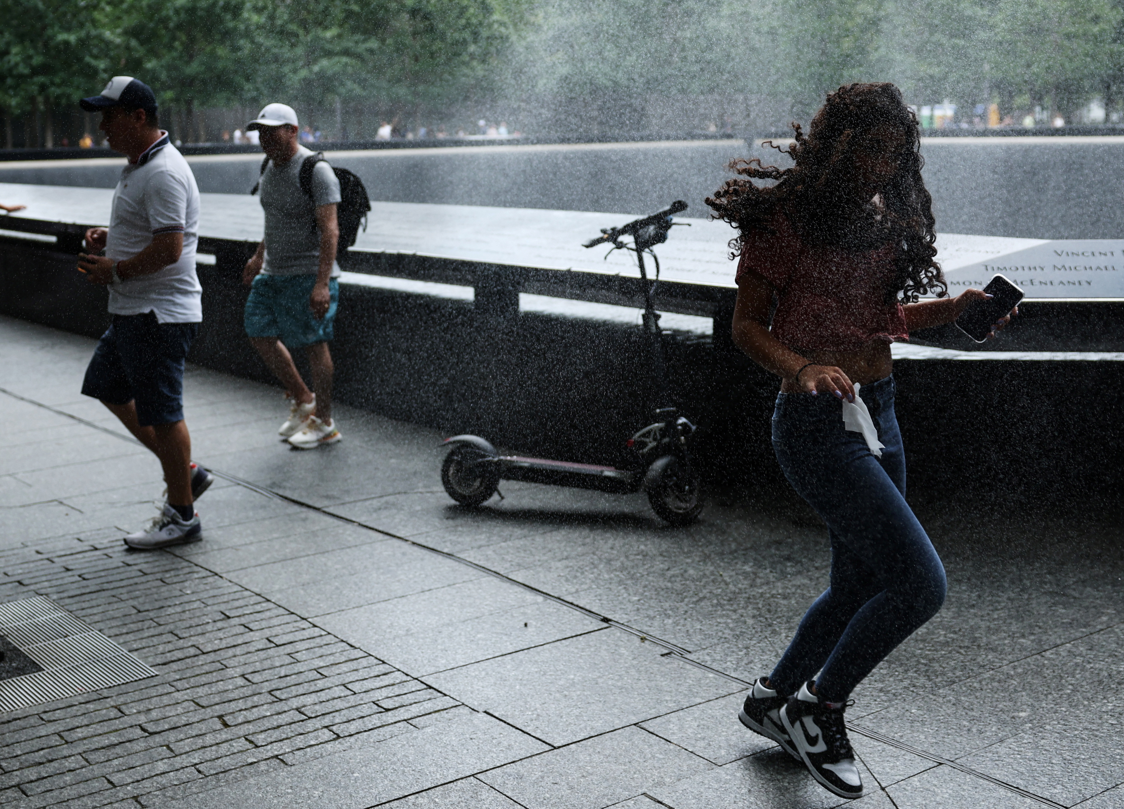 People cool off with a spray from the north reflecting pool at the 911 Memorial and Museum, after New York City issued an excessive heat warning, during hot windy weather in lower Manhattan in New York City, New York, U.S., July 27, 2023. REUTERS/Mike Segar