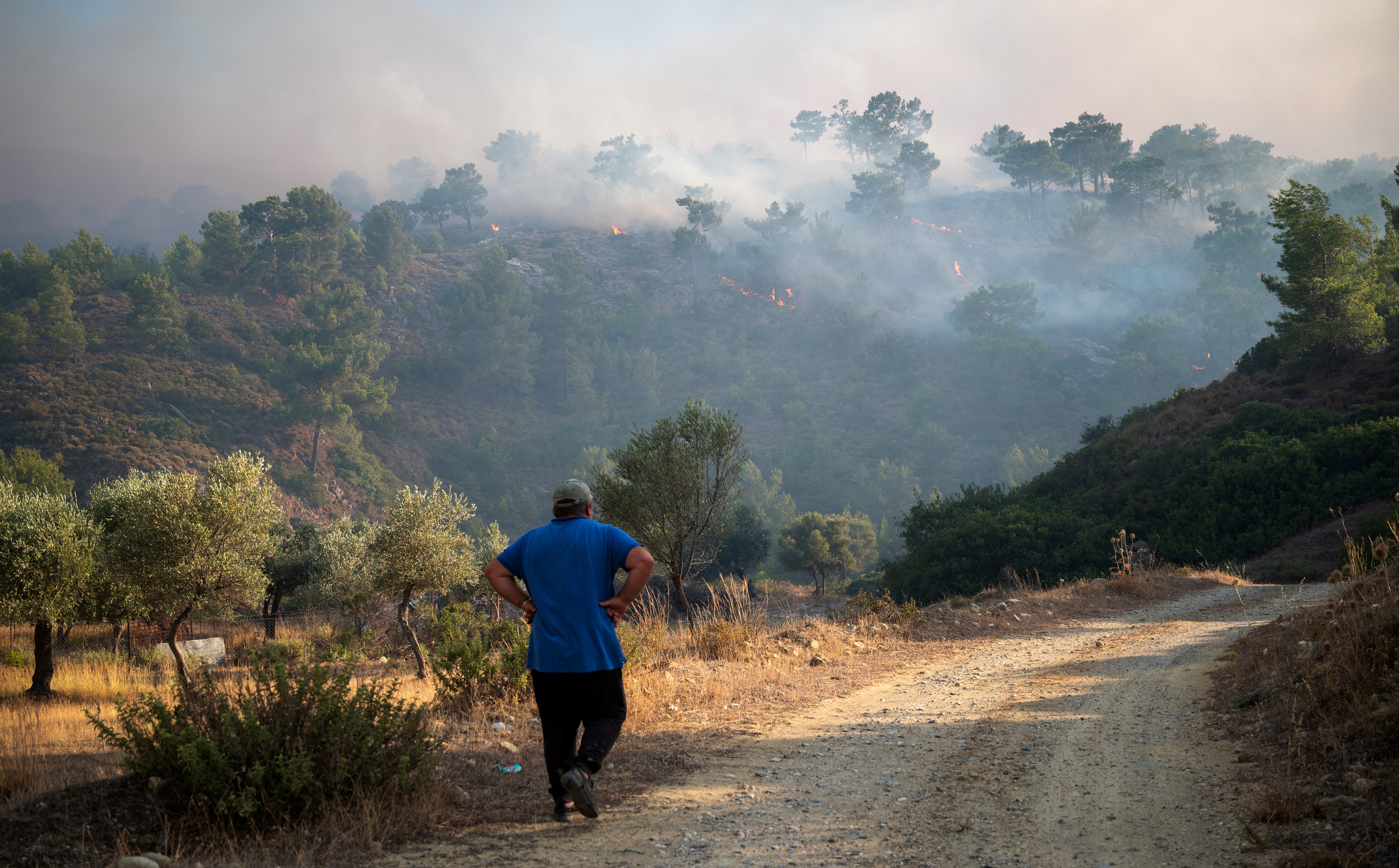 A man walks on a road, as wildfire burns near Lardos, on the island of Rhodes, Greece, July 22, 2023. REUTERS/Vassilis Ikoutas