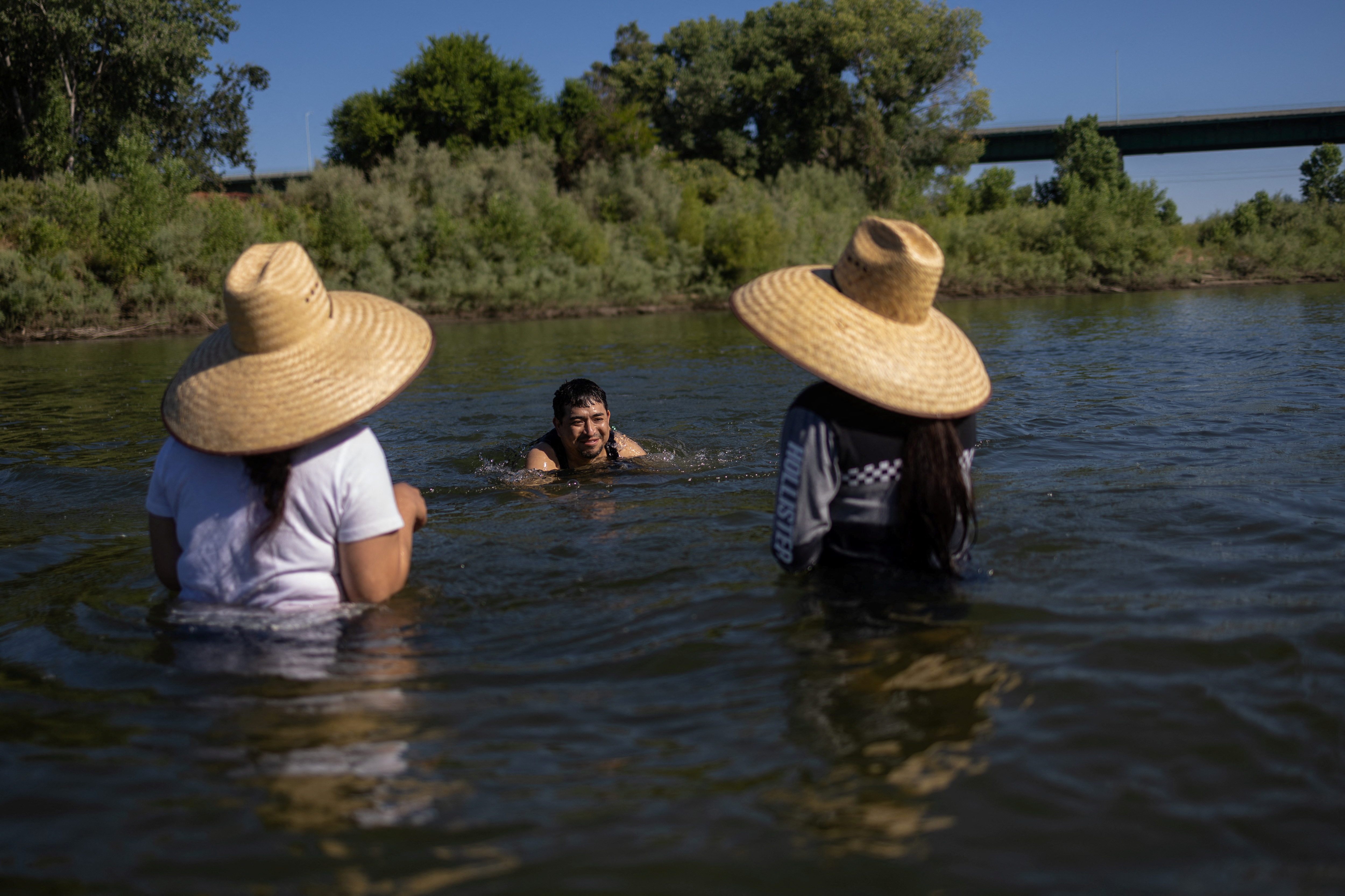 Cristian, Mari, and Sonia, migrant workers from Hidalgo, Mexico, refresh themselves after a day on the fields at the Feather River, as the temperature rises over 100 degrees Fahrenheit (38 Celsius), in Yuba City, California, U.S., June 30, 2023. REUTERS/Carlos Barria