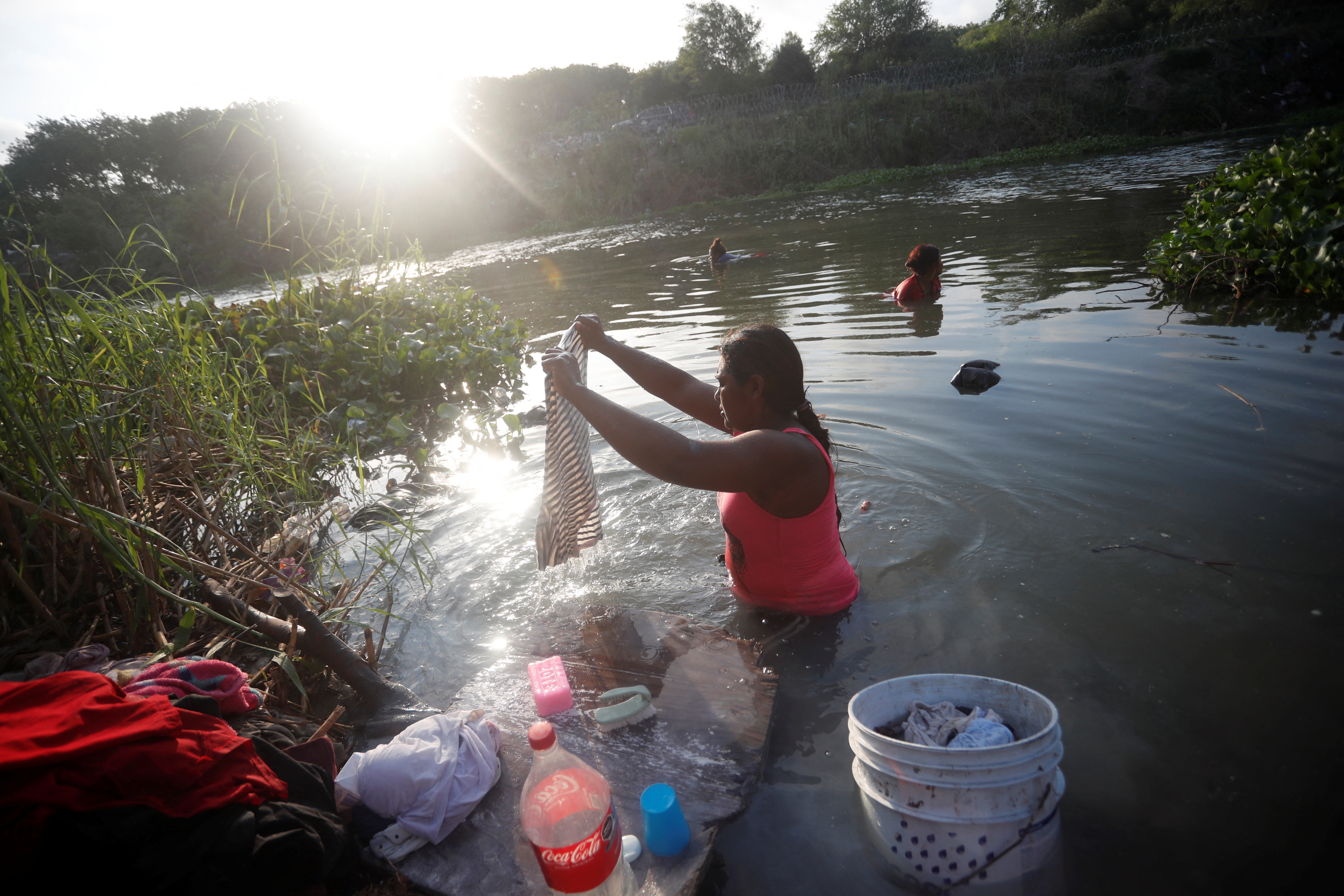 An asylum seeker washes her clothes in the Rio Grande river while she waits to attempt to cross into the U.S. by an appointment through the Customs and Border Protection app, called CBP One, at a makeshift camp, in Matamoros, Mexico June 21, 2023. President Joe Biden promised to replace the hardline policies of former President Donald Trump, including the COVID-era public health order Title 42, with a more humane immigration system. The new Biden regulation allows migrants once again to ask for asylum at the border, but wait in Mexico for a slot on the app or risk a sped-up deportation process that could be conducted while they are held in detention. But in the first month of the new policy, Reuters found tens of thousands of people are waiting in dangerous Mexican border towns to snag a spot on the app, according to U.S. and Mexican officials, amid warnings from humanitarian groups of deteriorating sanitary conditions at migrant camps. REUTERS/Daniel Becerril