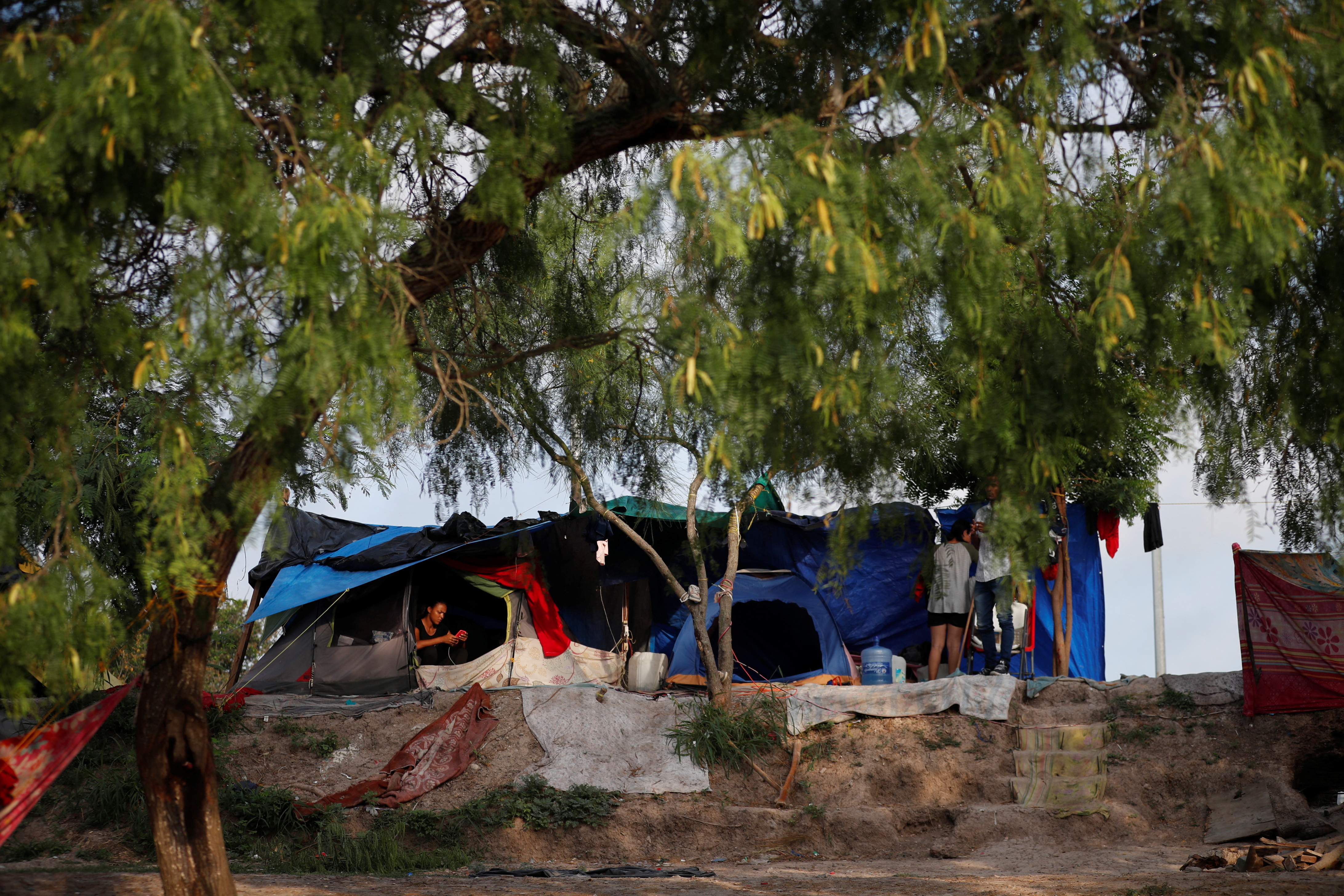 An asylum seeker checks her cellphone inside her tent as she waits to attempt to cross into the U.S. by an appointment through the Customs and Border Protection app, called CBP One, at a makeshift camp, in Matamoros, Mexico June 21, 2023. President Joe Biden promised to replace the hardline policies of former President Donald Trump, including the COVID-era public health order Title 42, with a more humane immigration system. The new Biden regulation allows migrants once again to ask for asylum at the border, but wait in Mexico for a slot on the app or risk a sped-up deportation process that could be conducted while they are held in detention. But in the first month of the new policy, Reuters found tens of thousands of people are waiting in dangerous Mexican border towns to snag a spot on the app, according to U.S. and Mexican officials, amid warnings from humanitarian groups of deteriorating sanitary conditions at migrant camps. REUTERS/Daniel Becerril
