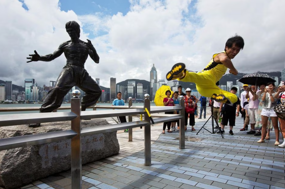 Chinese actor Mei Zhiyong performs a flying kick in front of a bronze statue of kung fu legend Bruce Lee on the waterfront of Hong Kong, July 20, 2013.