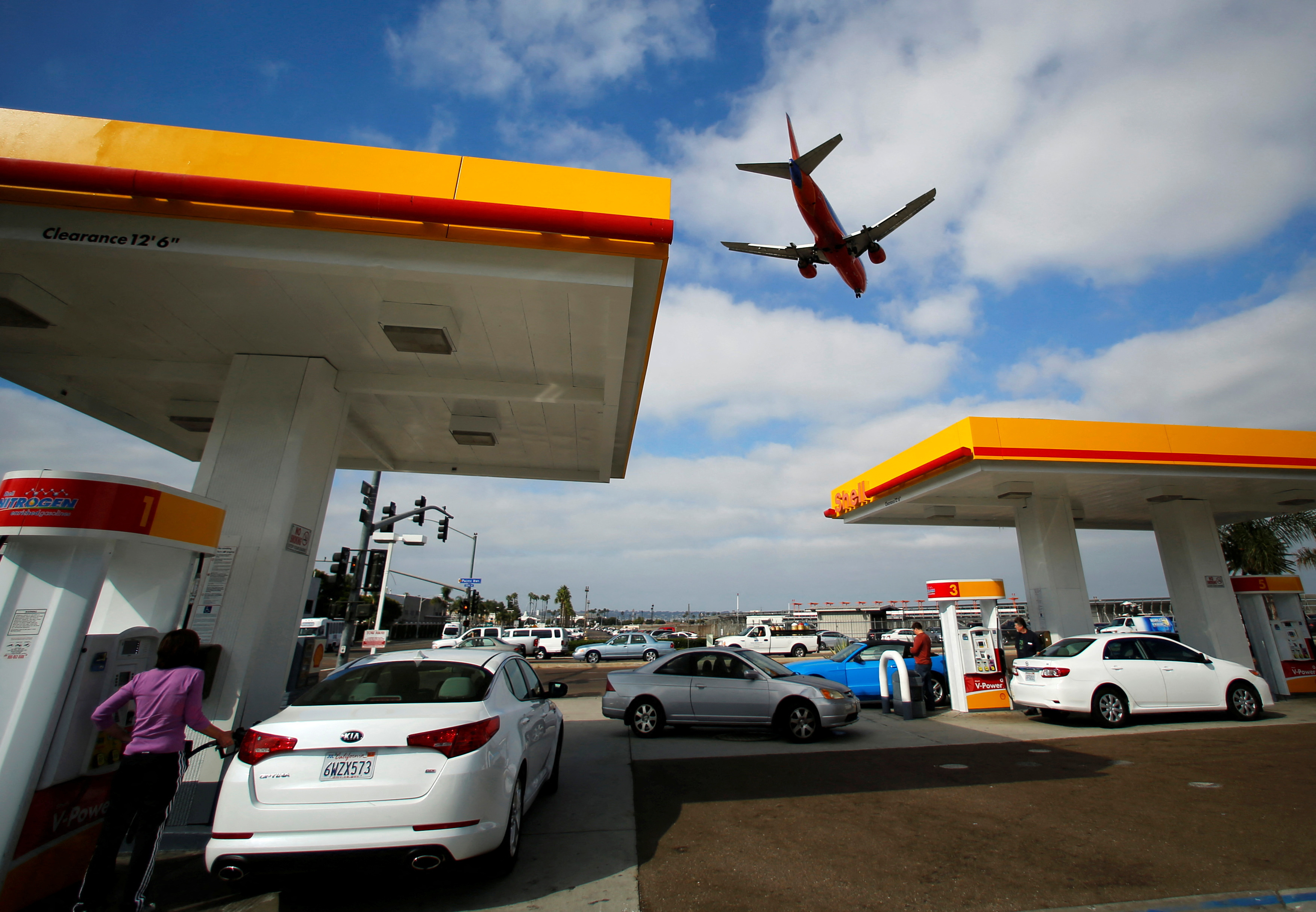 Consumers purchase gasoline at a gas station as a plane approaches to land at the airport in San Diego, California October 8, 2012. REUTERS/Mike Blake/File Photo