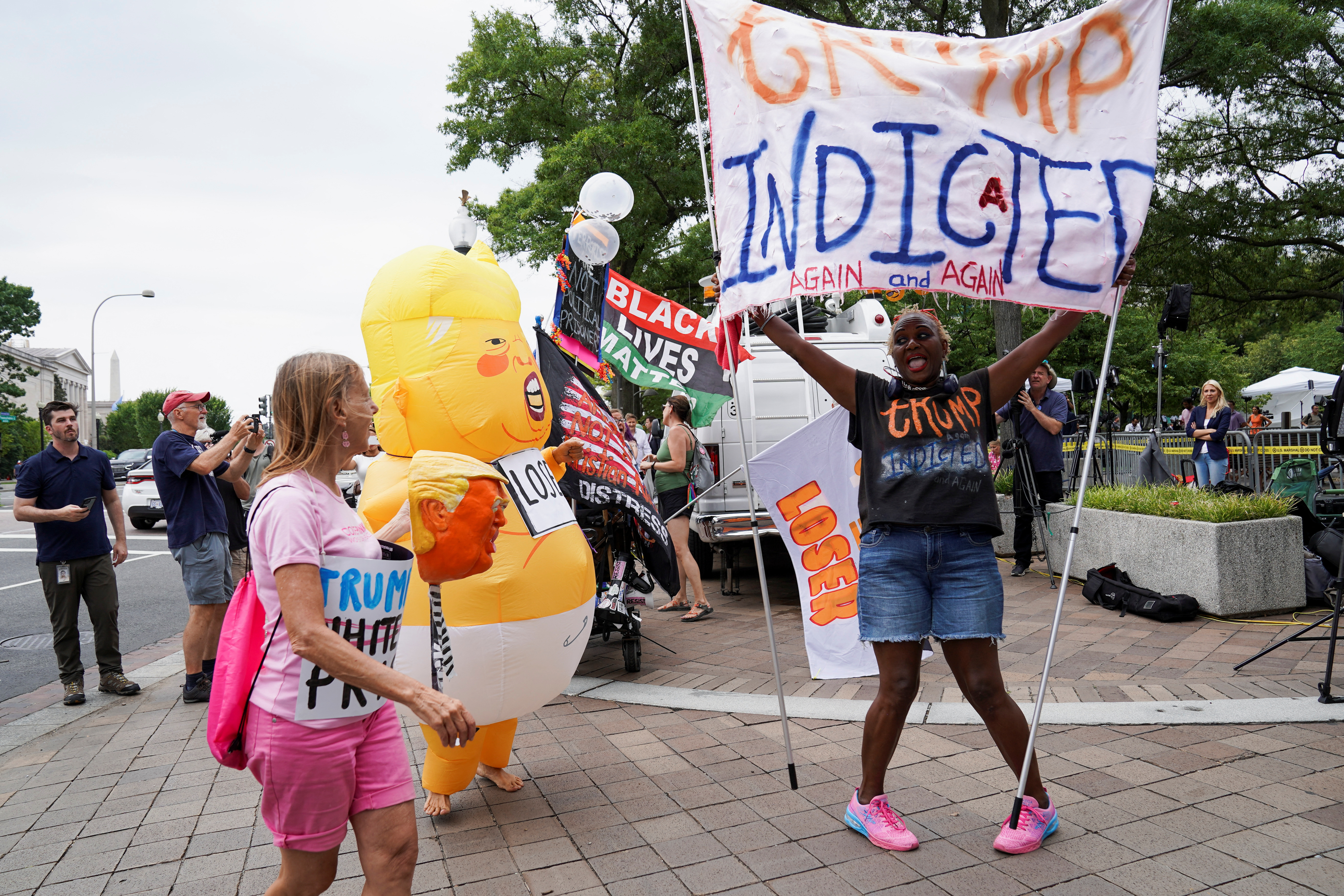 A demonstrator holds a banner, while standing near a person wearing a Baby Trump costume, as people gather on the day former U.S. President Donald Trump, who is facing federal charges related to attempts to overturn his 2020 election defeat, appears at the U.S. District Court in Washington, U.S., August 3, 2023. REUTERS/Sarah Silbiger