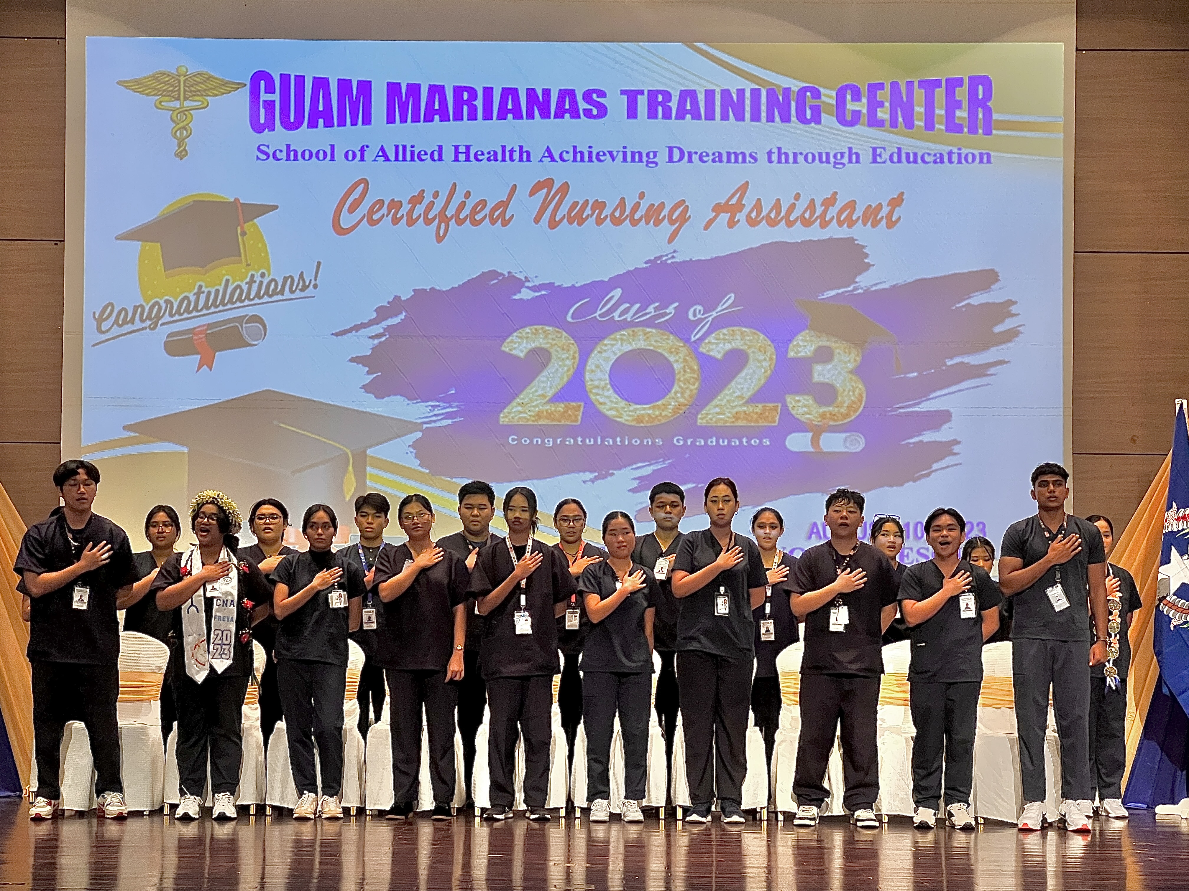 The 21 students who completed the Public School System-Guam Marianas Training Center Nursing Assistant Program sing the national anthem: Saim Ali (Tinian Jr.-Sr. High School), John L. Apit (Marianas High School), Kevin Bao (Mount Carmel School), Elizah Mae Canlas (Marianas High School), Serin Chung (Saipan International School), Jezreel Drilon (MHS), Joann Garcia (SSHS), Freya D. Greathouse (Dr. Rita H. Inos Jr.-Sr. High School), Xinwen Jin (MCS), Siena Lazaro (TJSHS), Kyla Charylle S. Macabanti (Northern Marianas College), Jamille Pangelinan (NMC), Kaeli Pathil (MHS), Joshua Revillame (MHS), Guillermina R. San Nicolas (TJSHS), Daryl Santiago (MHS), Kelvin Shrestha (TJSHS), Joana Nicole Signio (NMC), Elizah Mae Valdez (MHS), Bea Carmela Villafuerte (NMC), and Maria K. Cristobal (MHS).