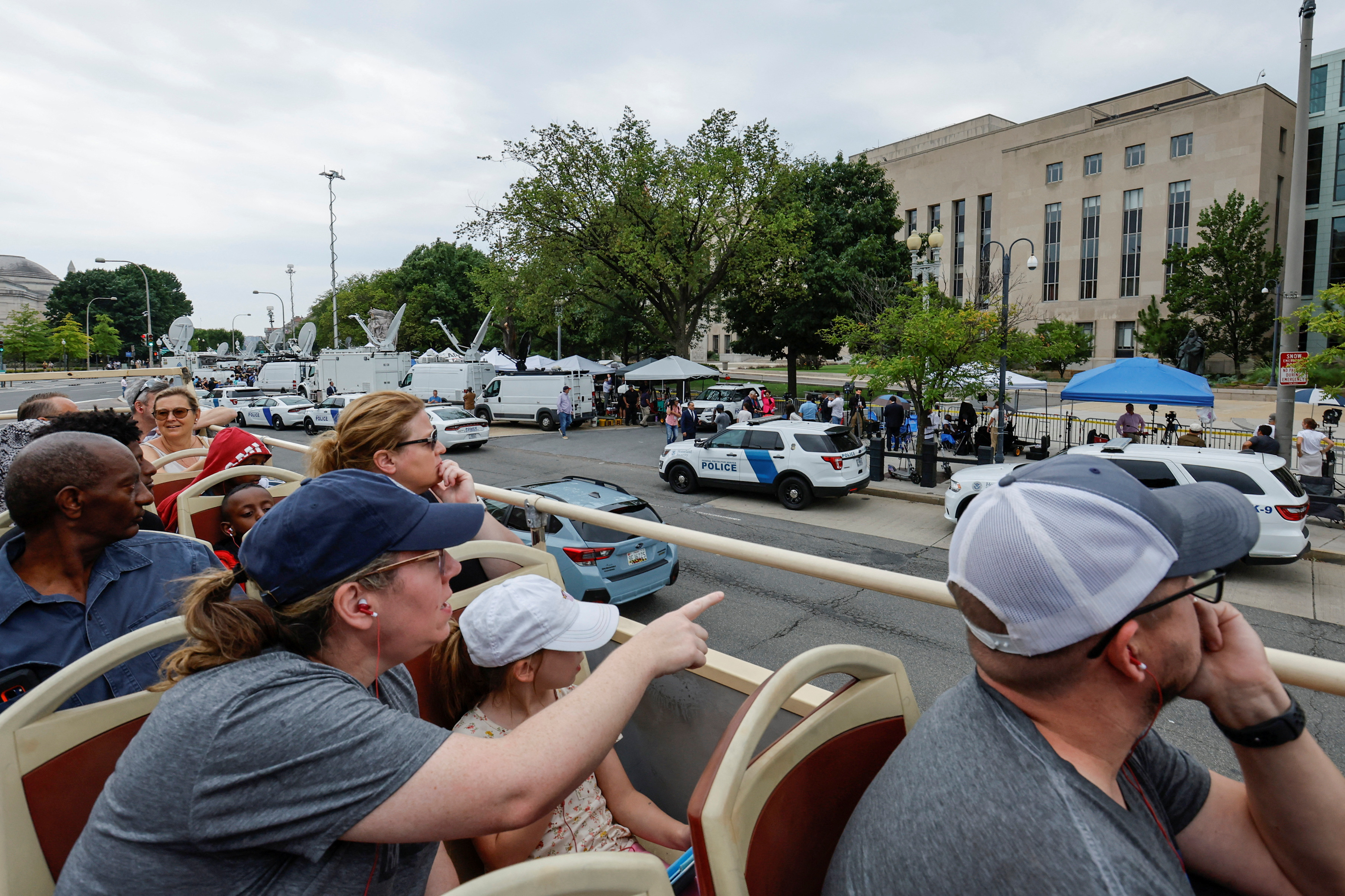 Tourists atop a double-decker tour bus pass by assembled reporters, law enforcement officers and demonstrators as they wait for former U.S. President Donald Trump, who is facing federal charges related to attempts to overturn his 2020 election defeat, to arrive at U.S. District Court in Washington, U.S., August 3, 2023. REUTERS/Jonathan Ernst