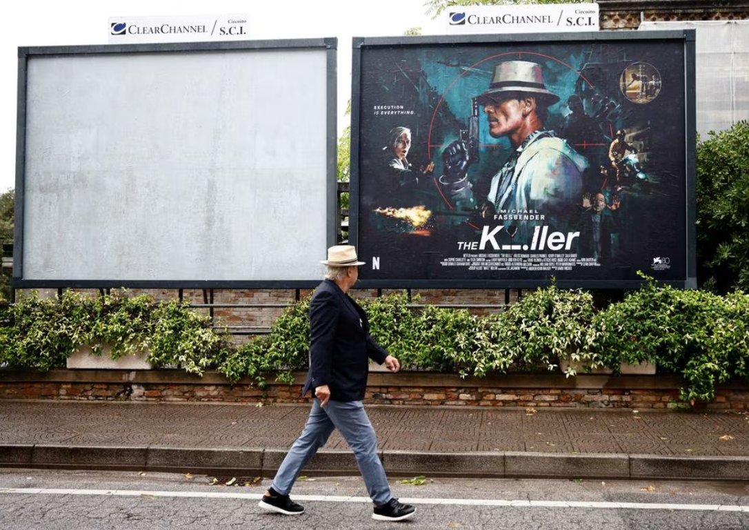 A man walks past a poster for the film "The Killer" on the eve of the opening ceremony of 80th Venice Film Festival, in Venice, Italy, Aug. 29, 2023.