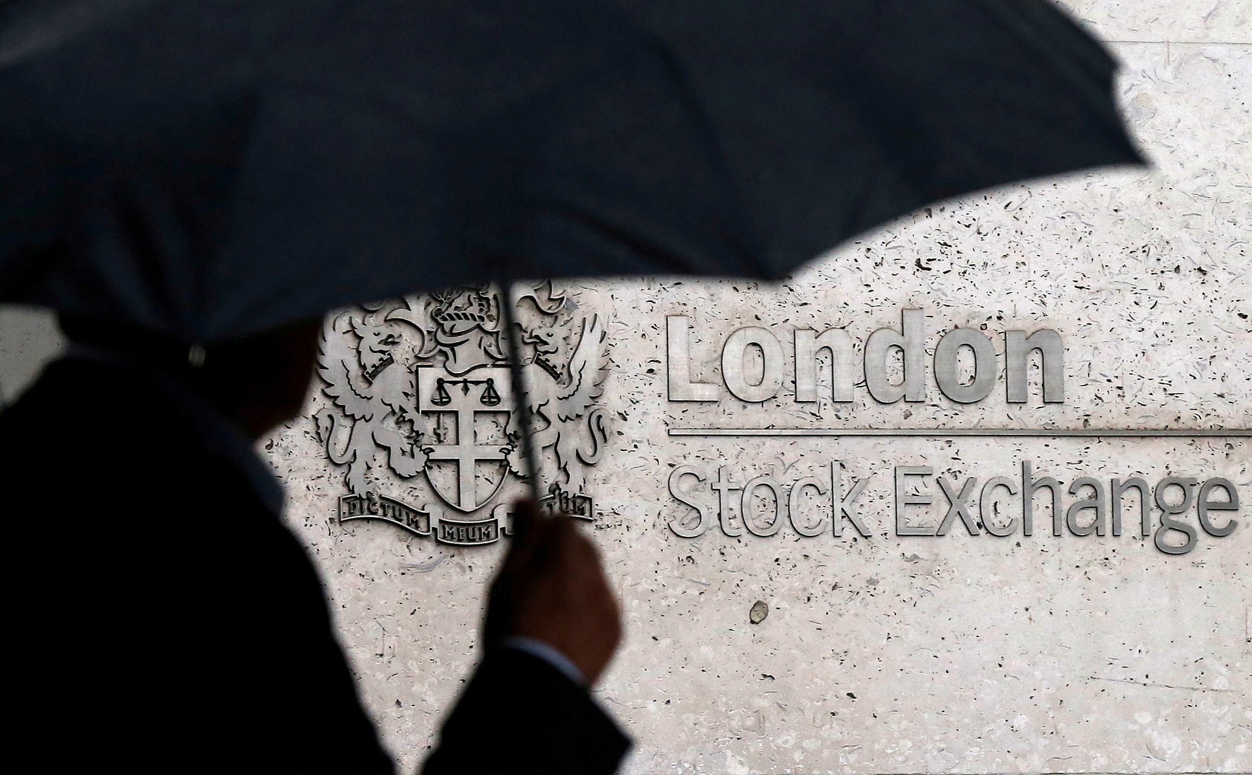 A man shelters under an umbrella as he walks past the London Stock Exchange  in London, Britain, Aug. 24, 2015.