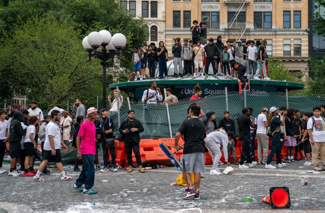 People stand on top of a subway station entrance to protect themselves after popular live streamer Kai Cenat announced a "giveaway" event that grew chaotic, prompting police officers to respond and disperse the crowd at Union Square and the surrounding streets, in New York City, Aug. 4, 2023.