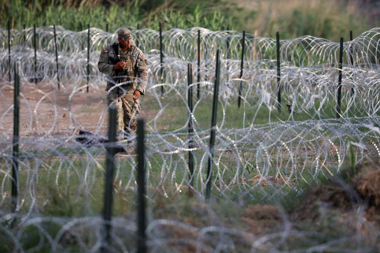 A Texas Army National Guard walks next to razor wire on the northern bank of the Rio Grande in Eagle Pass, Texas, U.S. May 23, 2022. U.S. authorities, blocked by a federal judge from lifting COVID-19 restrictions that empower agents at the U.S.-Mexico border to turn back migrants, continue to enforce the Title 42 rules which result in the fast expulsion of migrants to Mexico or other countries. REUTERS/Marco Bello