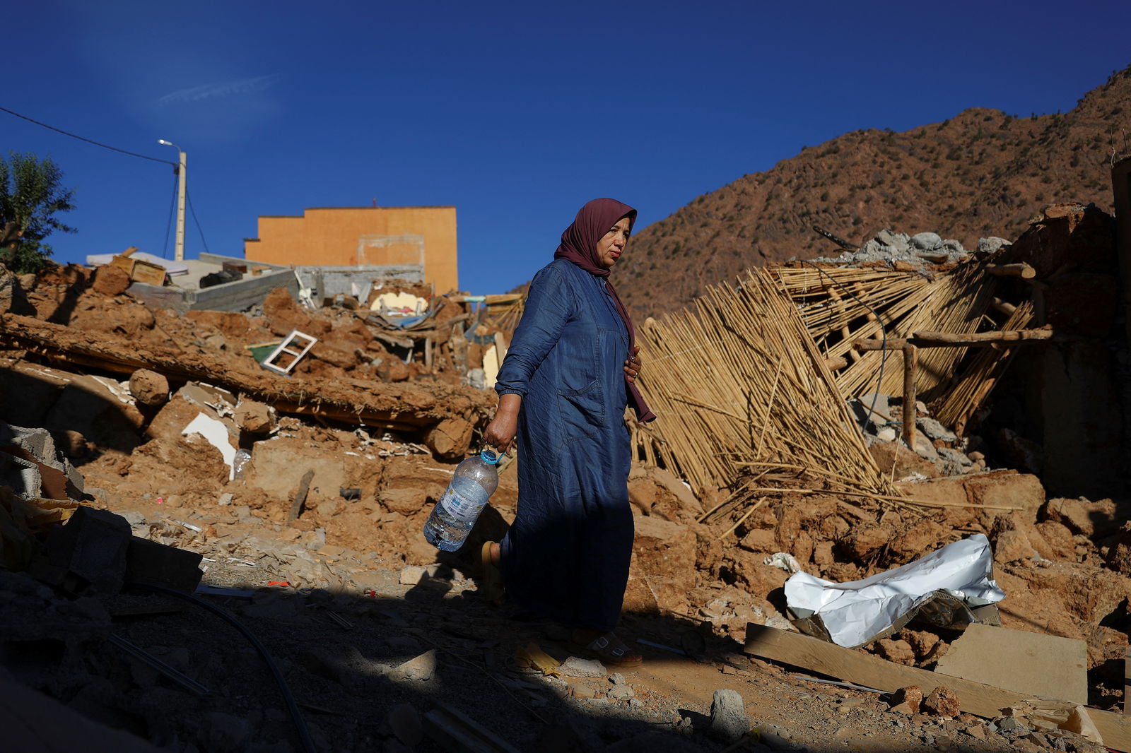 A woman carries a bottle, as she walks near rubble, in the aftermath of a deadly earthquake, in a hamlet on the outskirts of Talaat N'Yaaqoub, Morocco, September 11, 2023. REUTERS/Hannah McKay