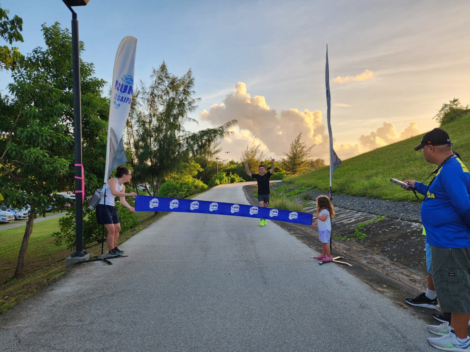 Jodie Sullivan celebrates as his wife and daughter hold the finish line during the 3rd Annual Run Saipan & Salty Skin Pacific 5K Run  at the Gov. Eloy S. Inos Peace Park on Friday.