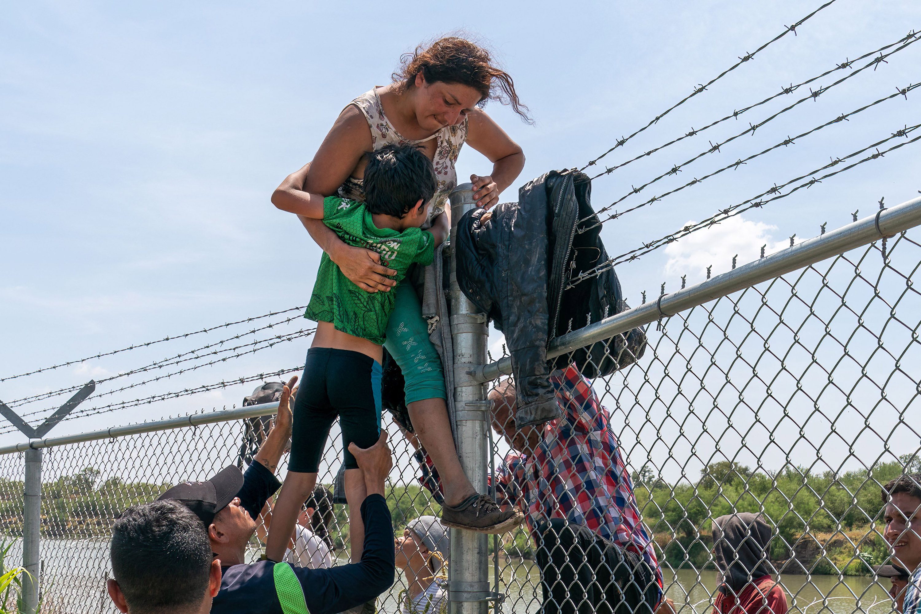 A mother helps her child over the barbed wire fence in Eagle Pass, Texas, after crossing into the U.S. from Mexico on Aug. 25, 2023. (Suzanne Cordeiro/AFP/Getty Images/TNS)