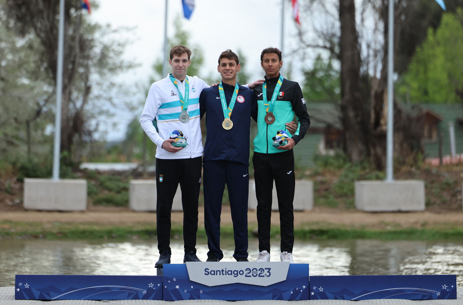 Pan-Am Games - Santiago 2023 - Open Water Swimming - Laguna Los Morros, Santiago, Chile - October 29, 2023 Gold medallist Brennan Gravley of the U.S. celebrates on the podium with his medal after winning the men's 10km final alongside Silver medallist Argentina's Franco Ivo Cassini and Bronze medallist Mexico's Paulo Strehlke Delgado.