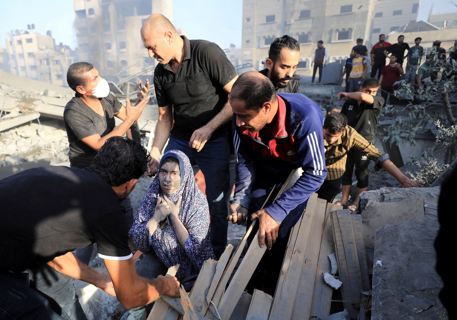 A Palestinian woman is assisted, as people search for casualties at the site of an Israeli strike on a residential building in Gaza City, October 25, 2023. 