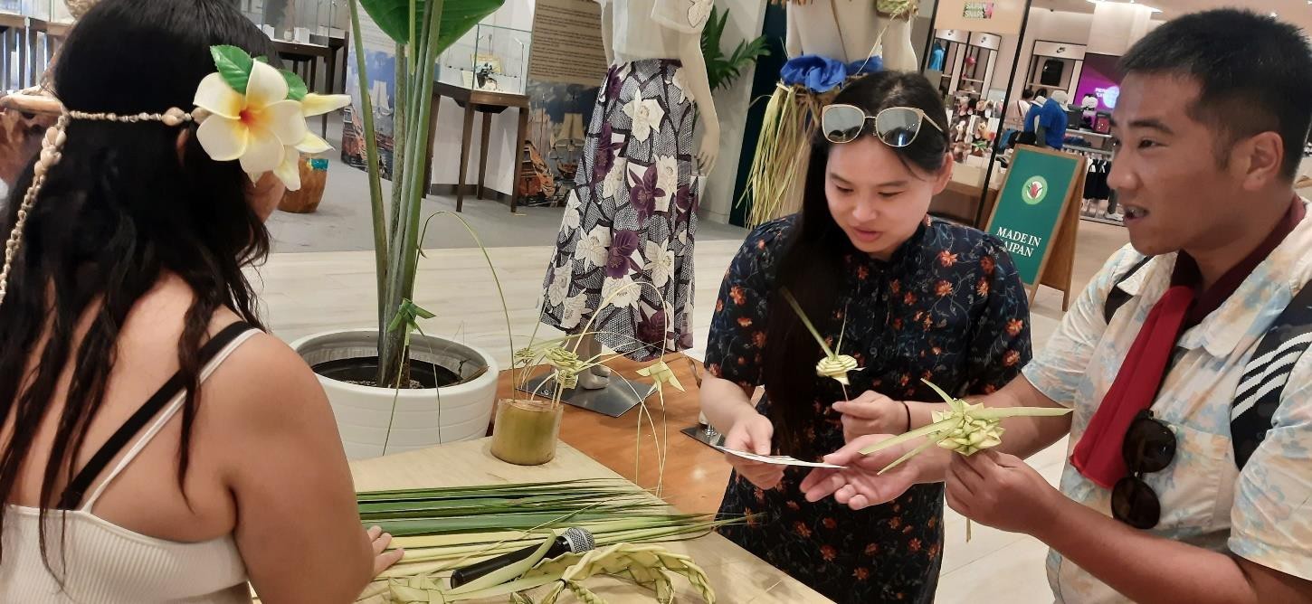 Visitors receive flowers woven from coconut fronds by Nicole Tyquiengco, left, on Sept. 28, 2023, at the Marianas Experience at T Galleria in Saipan.
