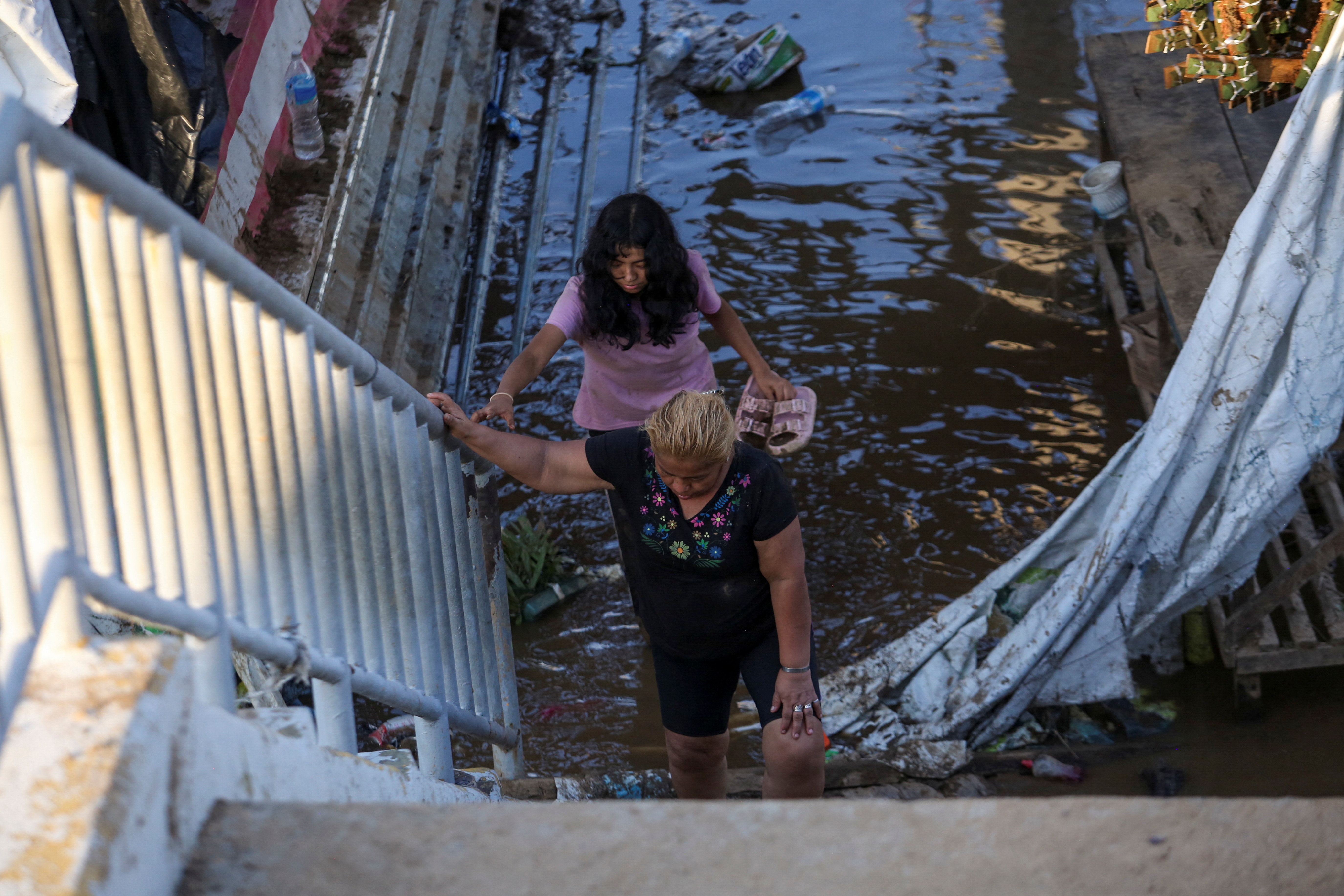 People climb stairs as they walk through an inundated street in the aftermath of Hurricane Otis, near Acapulco, Mexico, October 26, 2023. 