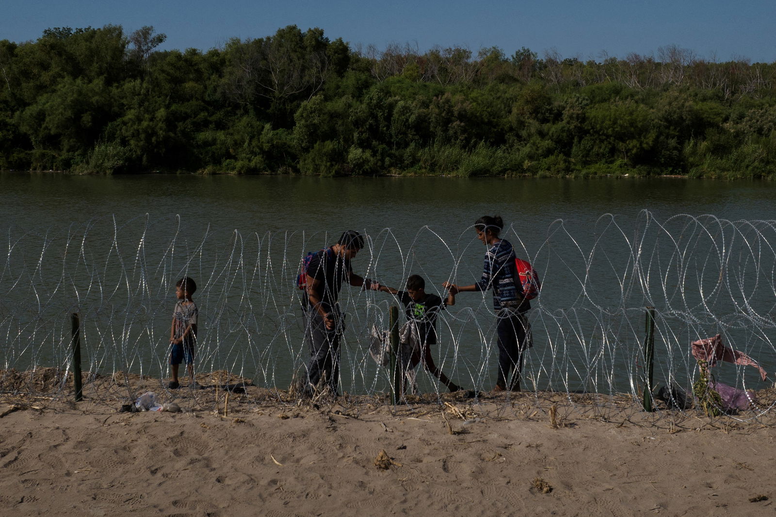 A family navigates the bank of the Rio Grande past razor wire while searching for an entry point into the United States from Mexico, in Eagle Pass, Texas, U.S. July 30, 2023. 