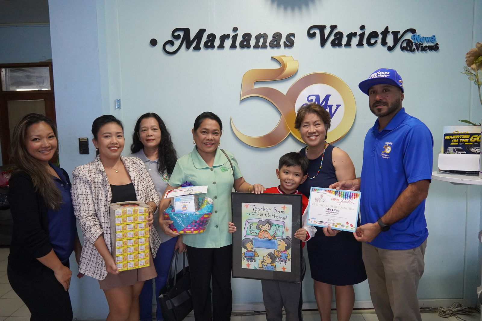 Second grader, Colin Lilles, is all smiles as he holds up his winning masterpiece while posing with his teacher, family and Variety staff.