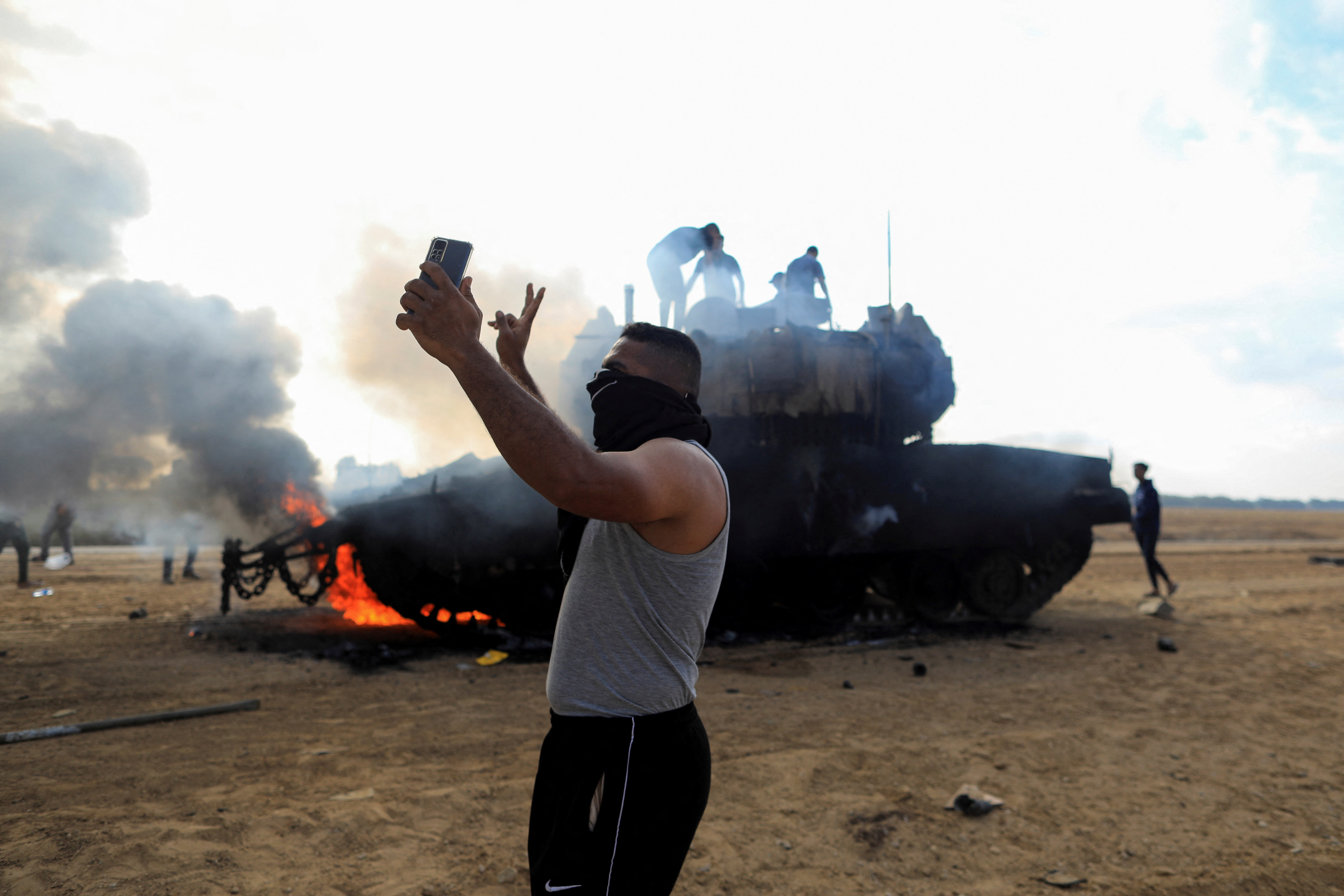 A Palestinian man takes a selfie in front of a burning Israeli military vehicle after it was hit by Palestinian gunmen who infiltrated areas of southern Israel, at the Israeli side of Israel-Gaza border, Oct. 7, 2023.