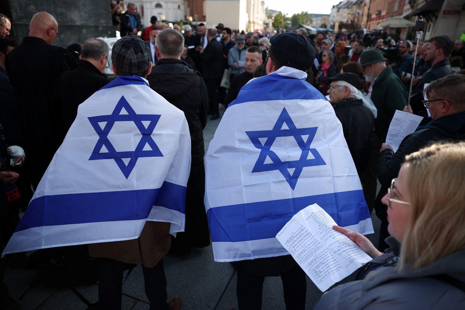 A man wrapped in the Israeli flag stands as a woman holds the text of prayer during multi-confessional prayer for peace after gunmen from Hamas entered Israeli territory on Saturday, at Old Town in Warsaw, Poland, October 13, 2023. REUTERS/Kacper Pempel