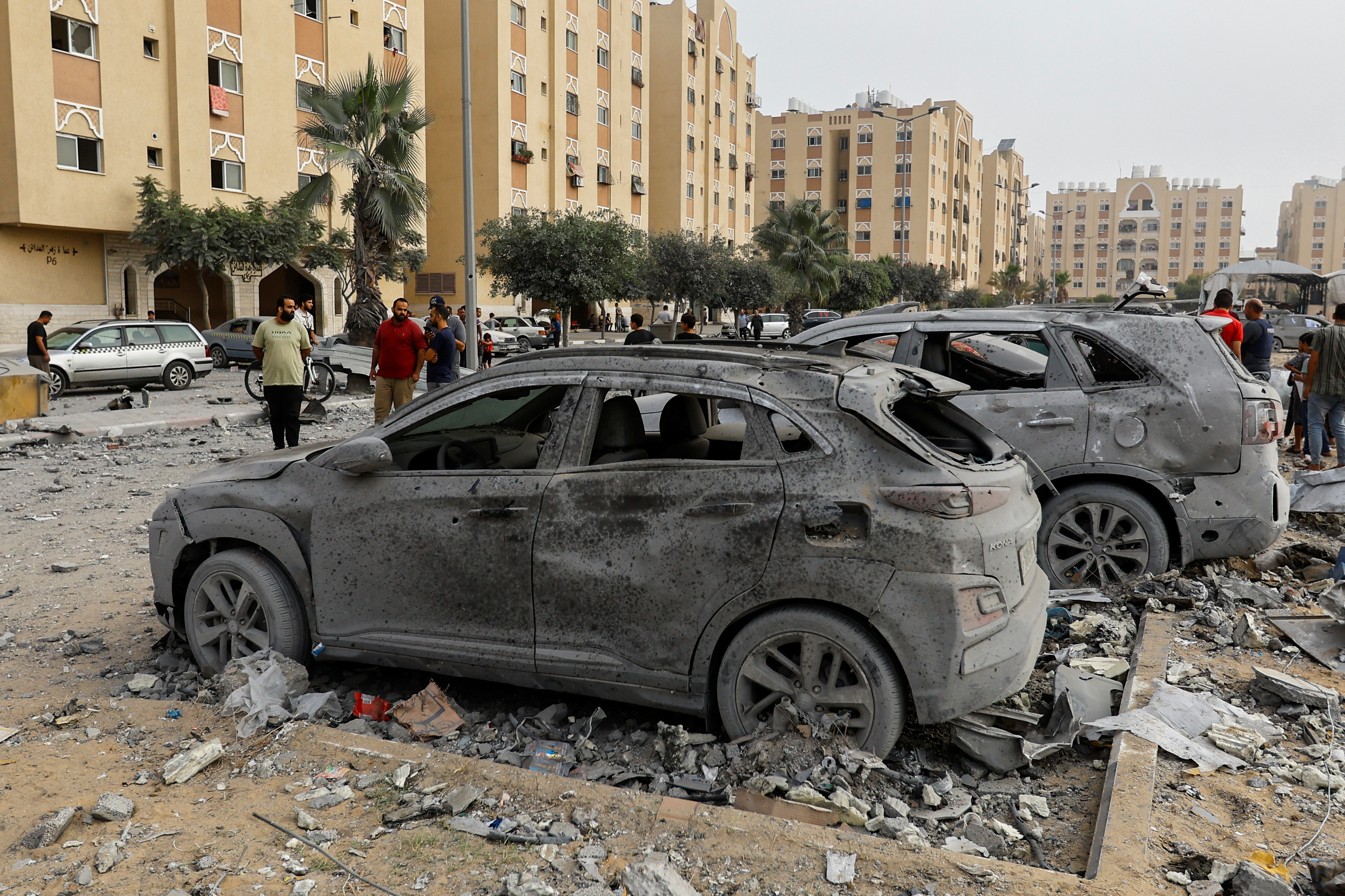 Palestinians look at damaged vehicles near the site of Israeli strikes on a house in Khan Younis in the southern Gaza Strip, October 23, 2023. 