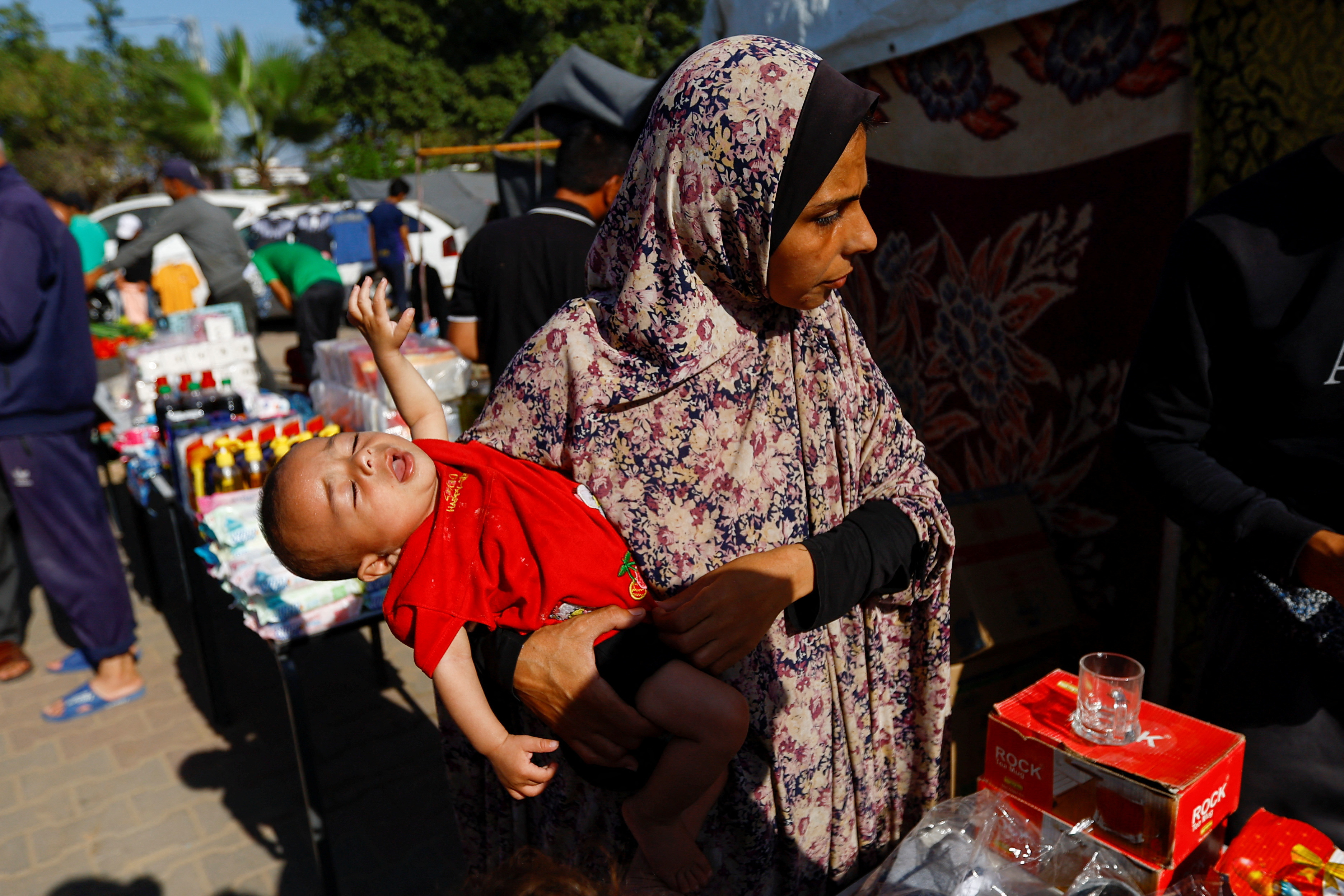 A Palestinian woman, who fled her house amid Israeli strikes, holds a child as they take shelter at a tent camp at a United Nations-run center, after Israel's call for more than 1 million civilians in northern Gaza to move south, in Khan Younis in the southern Gaza Strip, October 26, 2023. 