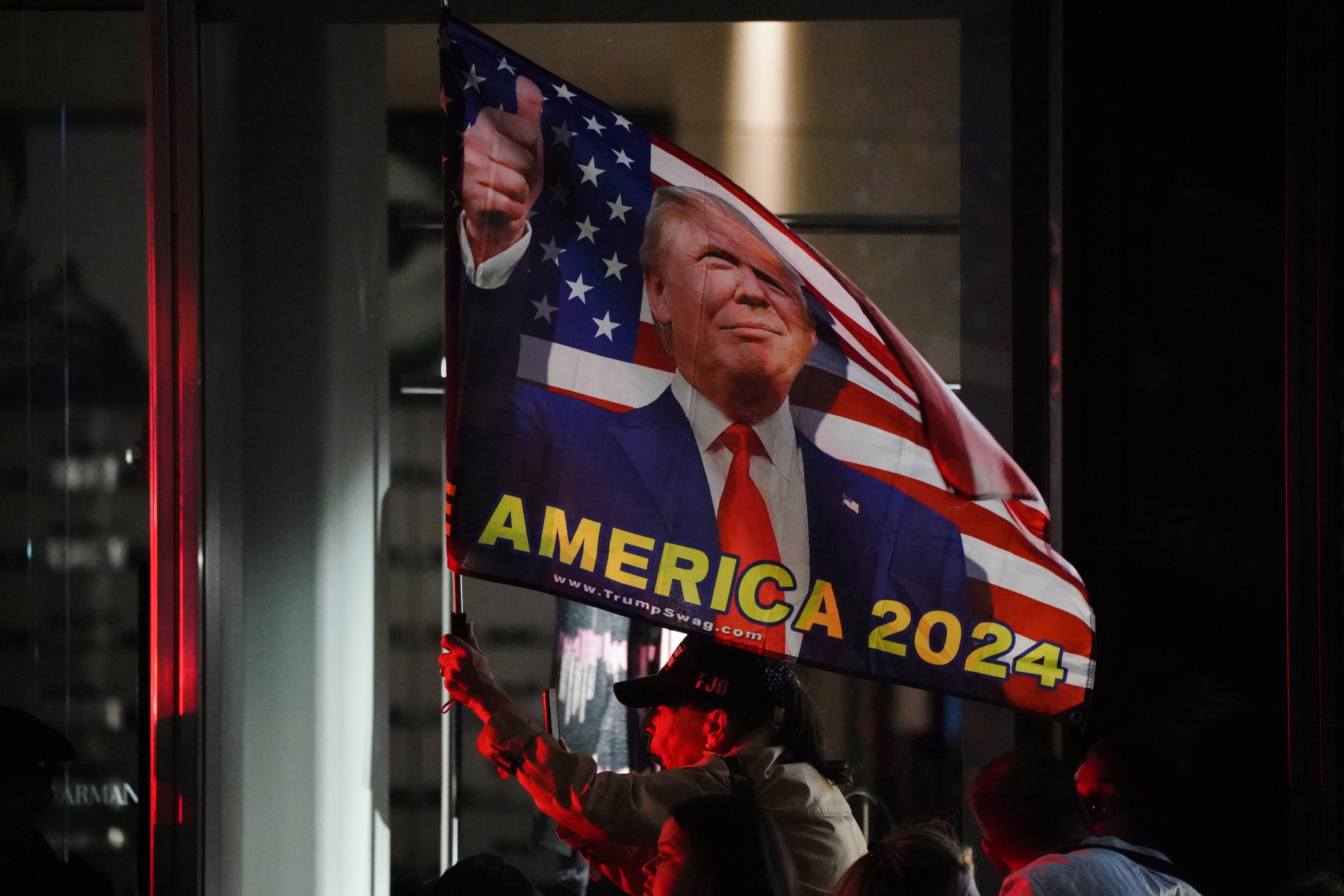 A supporter of former U.S. President Donald Trump waves an “America 2024” flag behind NYPD barricades at Trump Tower in New York City, U.S., October 1, 2023. 