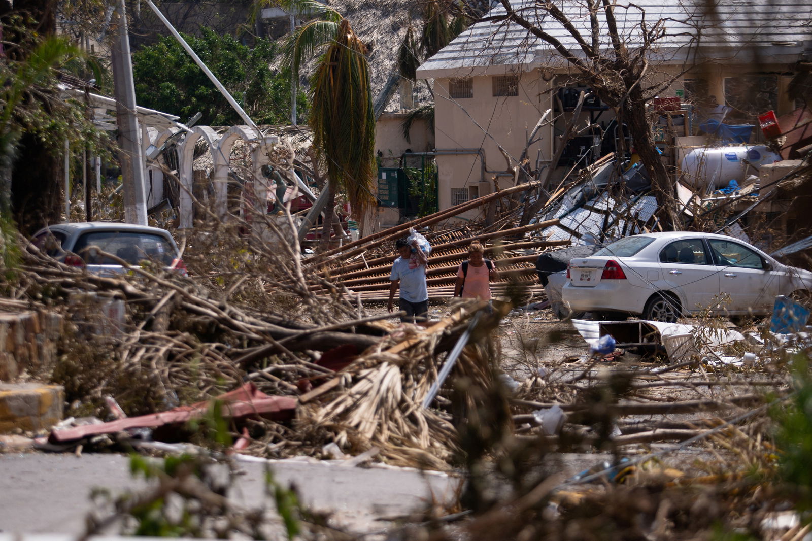 People walk next to rubble and damaged trees in the aftermath of Hurricane Otis, in Acapulco, Mexico, October 29, 2023.