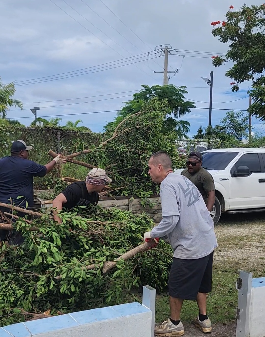 A police officer and inmates collect prunings for disposal.
