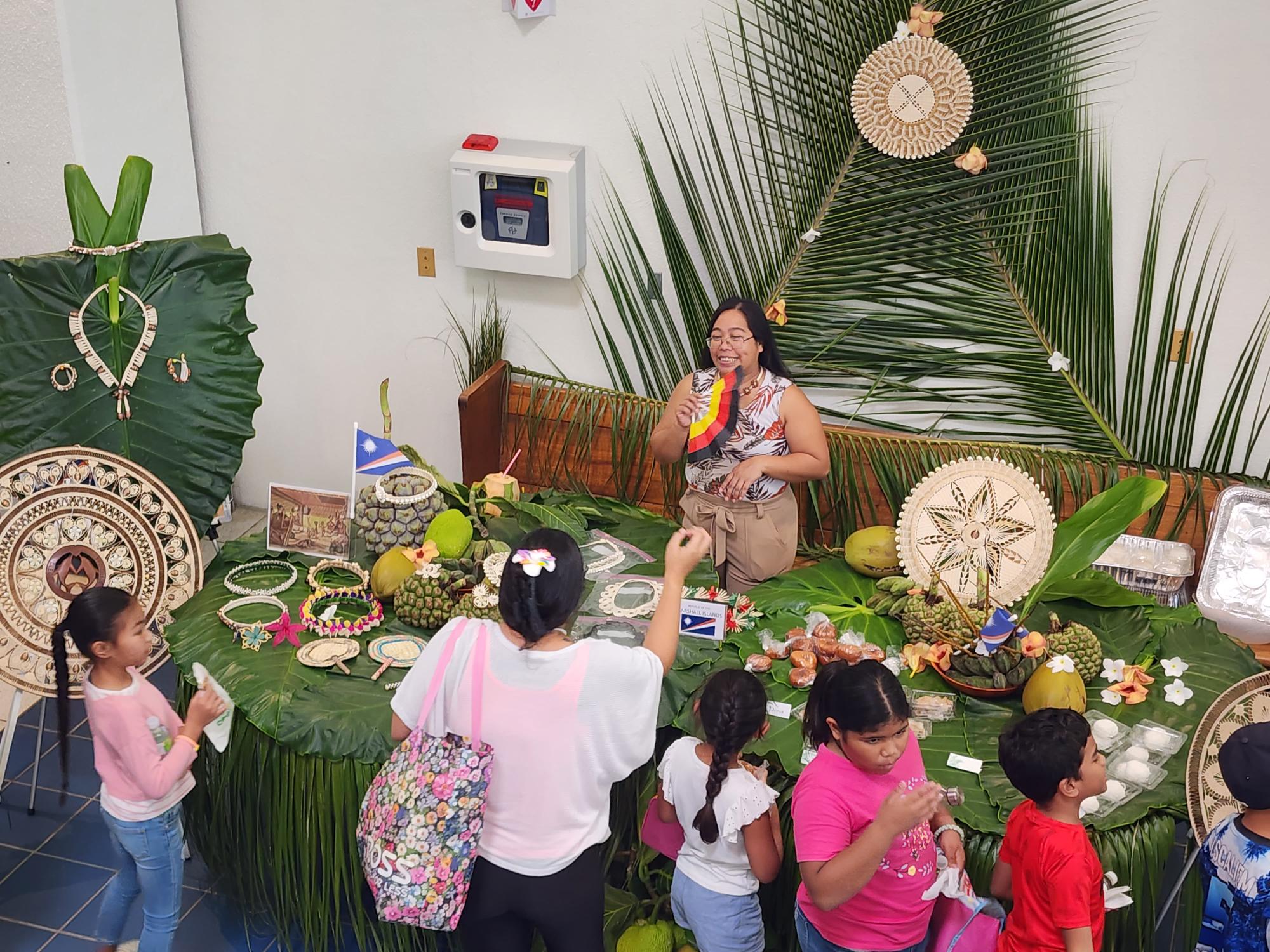 Deputy Clerk of Court Novelyn Tenorio discusses the Marshall Islands' culinary delicacies and handicrafts with a teacher and her students.