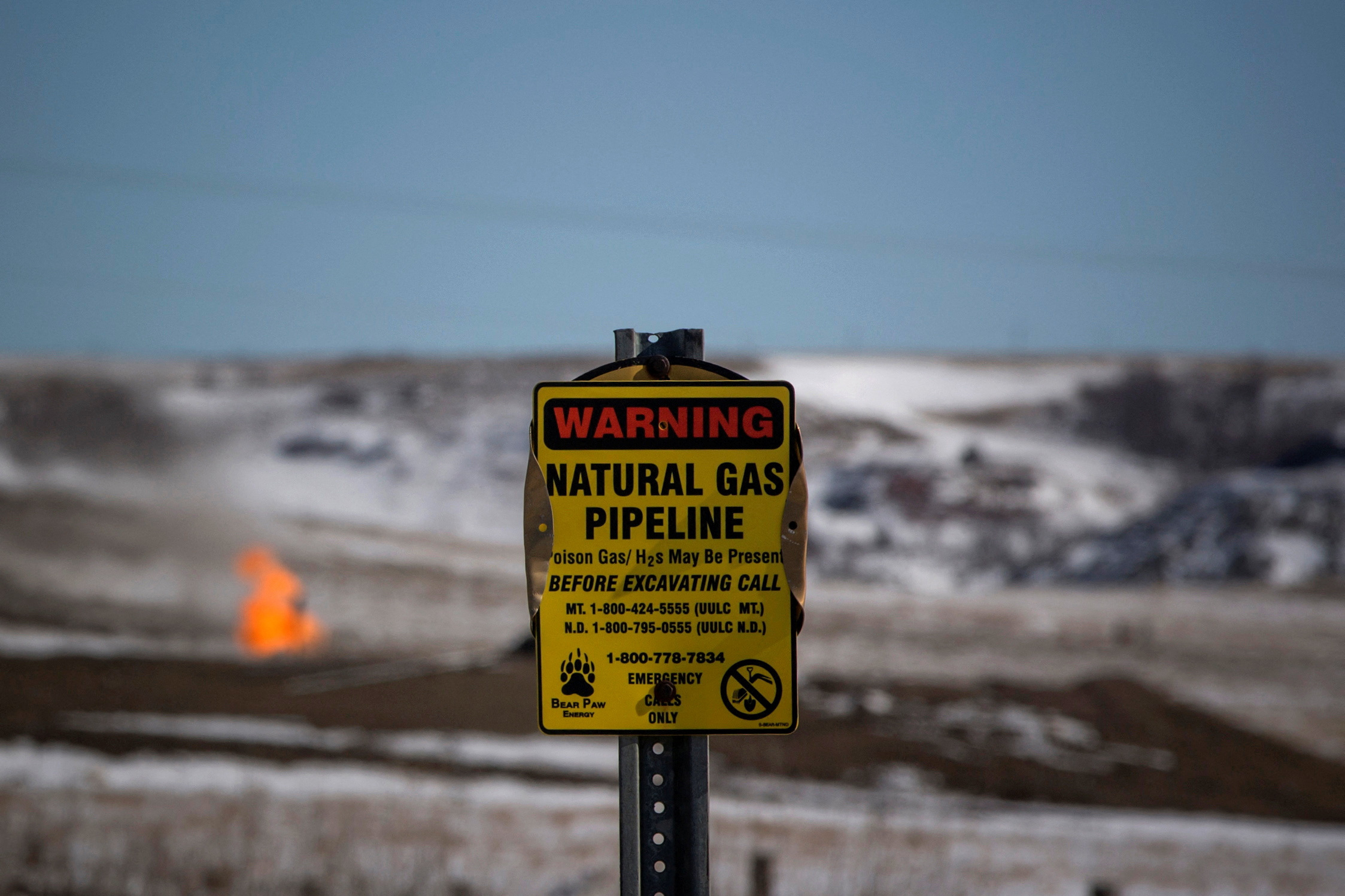 A warning sign for a natural gas pipeline is seen as natural gas flares at an oil pump site outside of Williston, North Dakota March 11, 2013. 