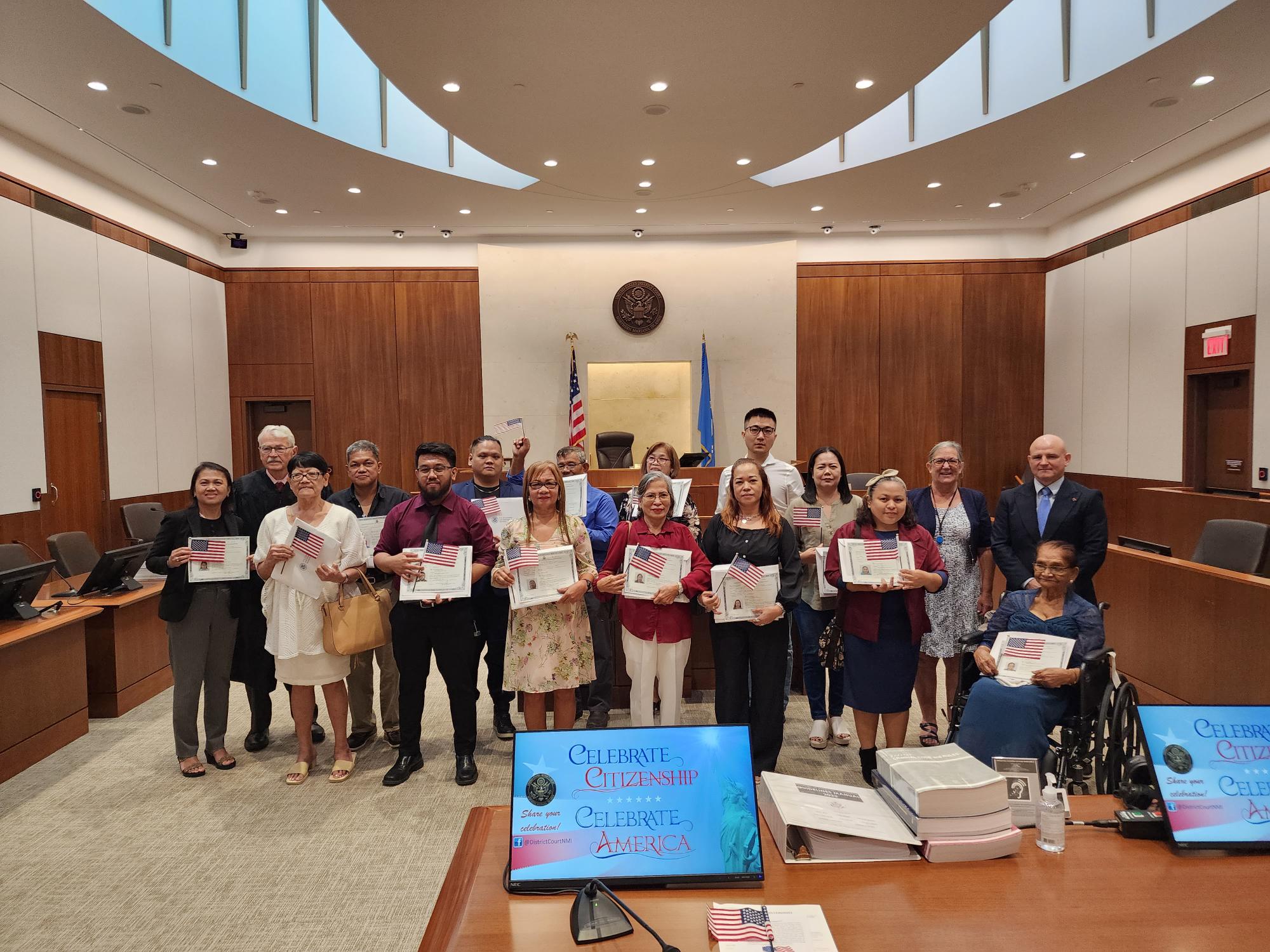 Senior Judge Alex R. Munson, 2nd left, poses with the 14 new U.S. citizens that he swore in Monday at the District Court for the NMI. Also in photo are attorney Joe McDoulett, the guest speaker, and U.S. Citizenship and Immigrations Services Officer Patricia Phelan.          