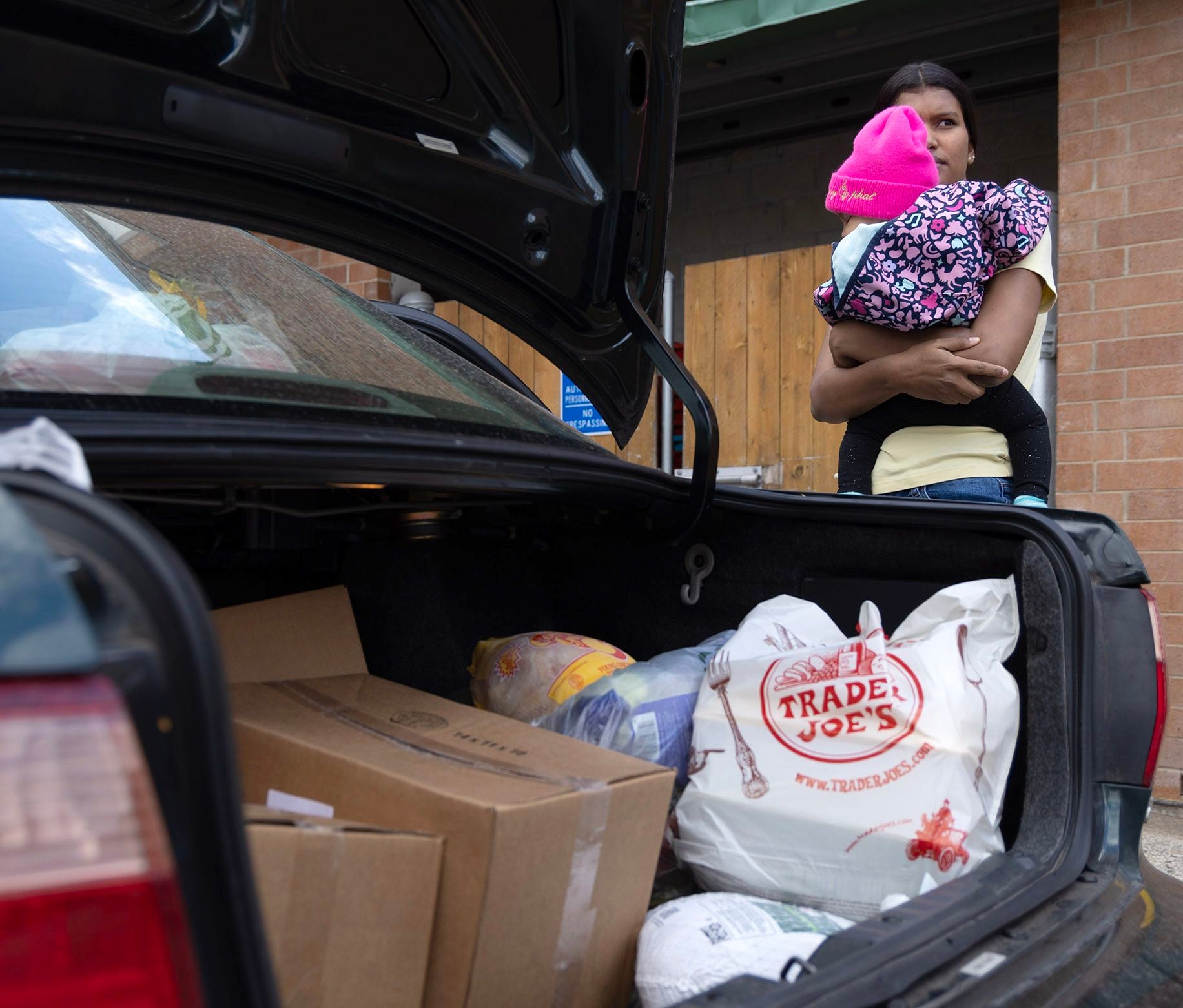 Venzuelan migrant Yorkaris Bello and her 7-month-old daughter, Jormaris, stand next to a car with food they and other families received from Nourishing Hope in Chicago on Nov. 10, 2023.