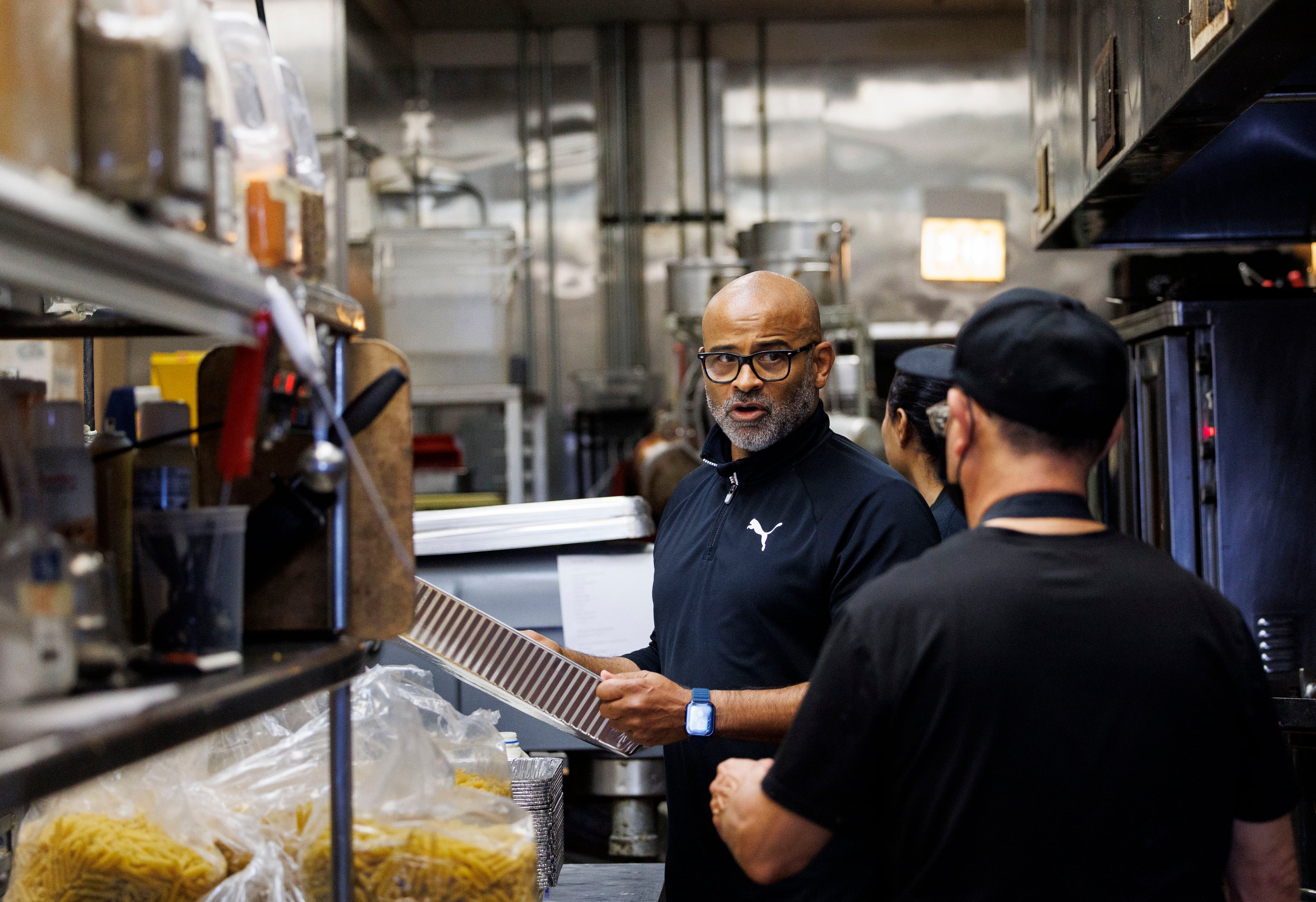 Owner John Meyer talks Mariana Vavalla, 29, a migrant from Venezuela, while working in the kitchen at BJ’s Market in the South Deering neighborhood on Nov. 7, 2023.