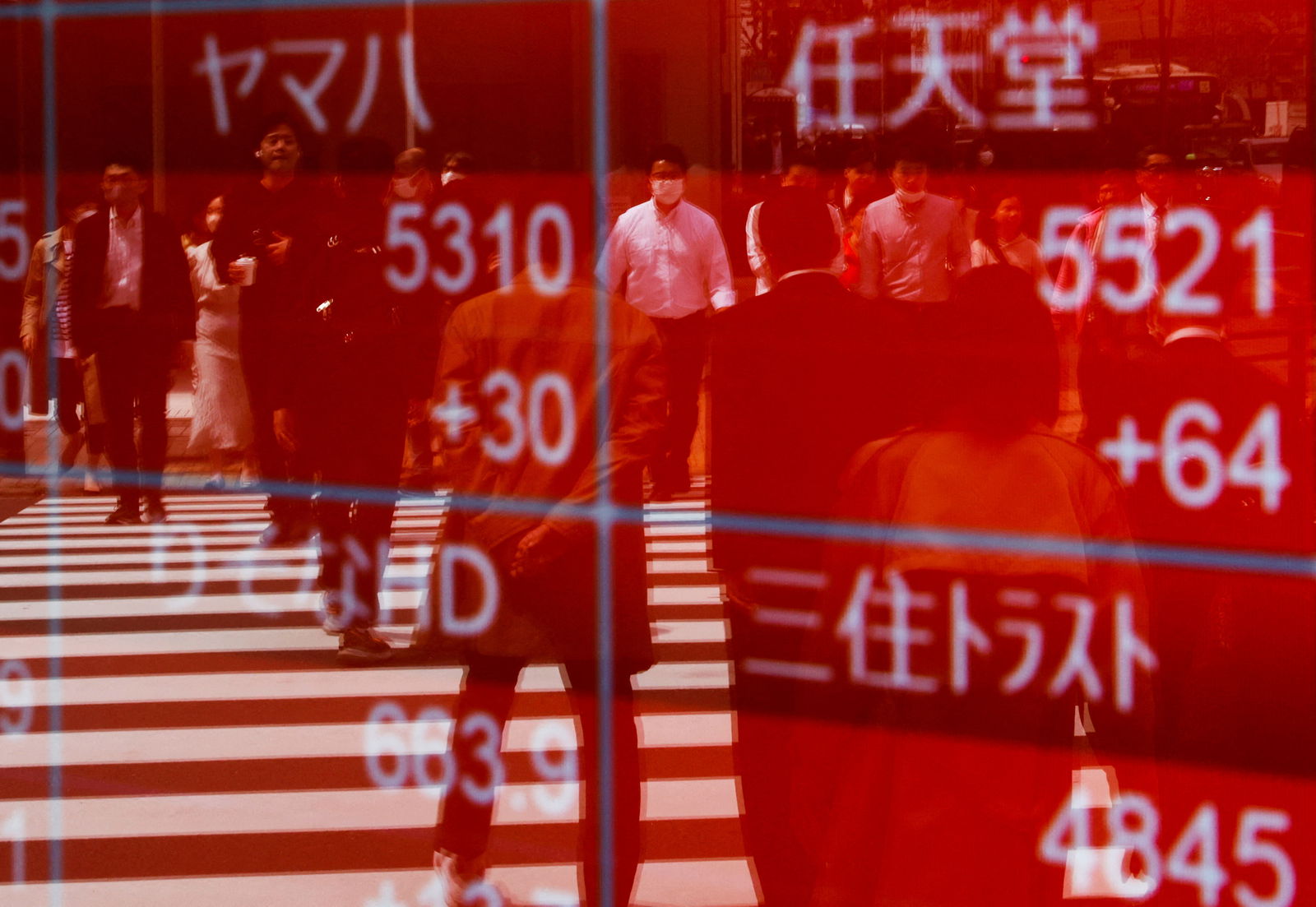 Passersby are reflected on an electric stock quotation board outside a brokerage in Tokyo, Japan, April 18, 2023.