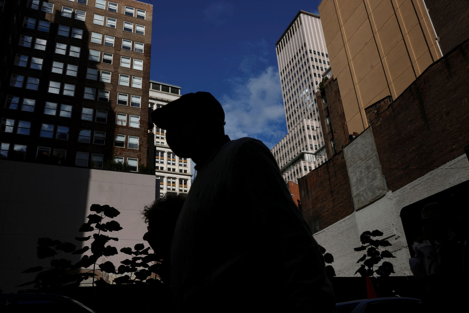 A man is seen silhouetted wearing a protective face mask, amid the coronavirus disease pandemic, as he walks near the financial district of New York City, Oct. 18, 2021.
